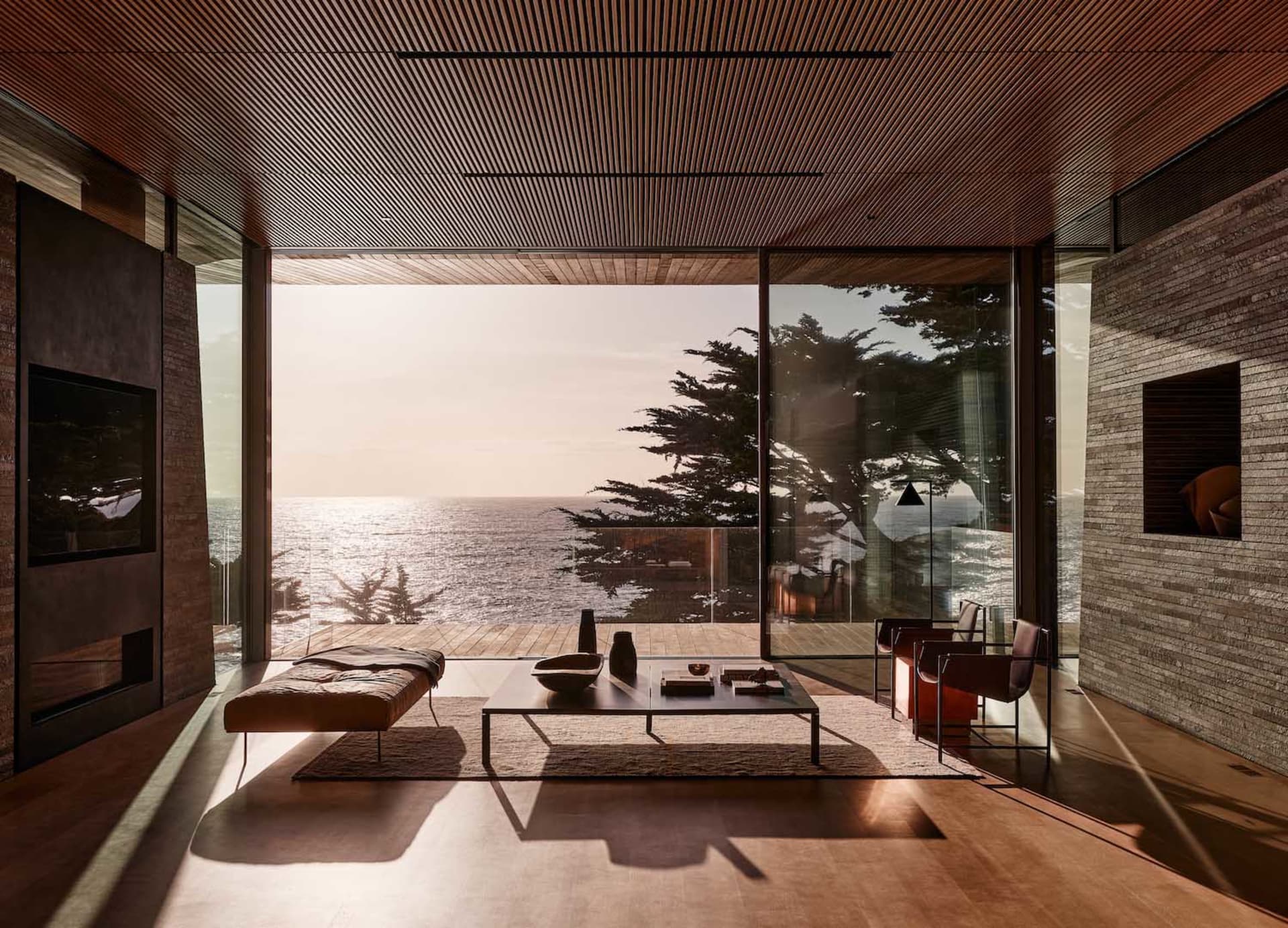 Modern living room with wooden flooring, furniture, and ceiling panels, featuring a stunning ocean view.