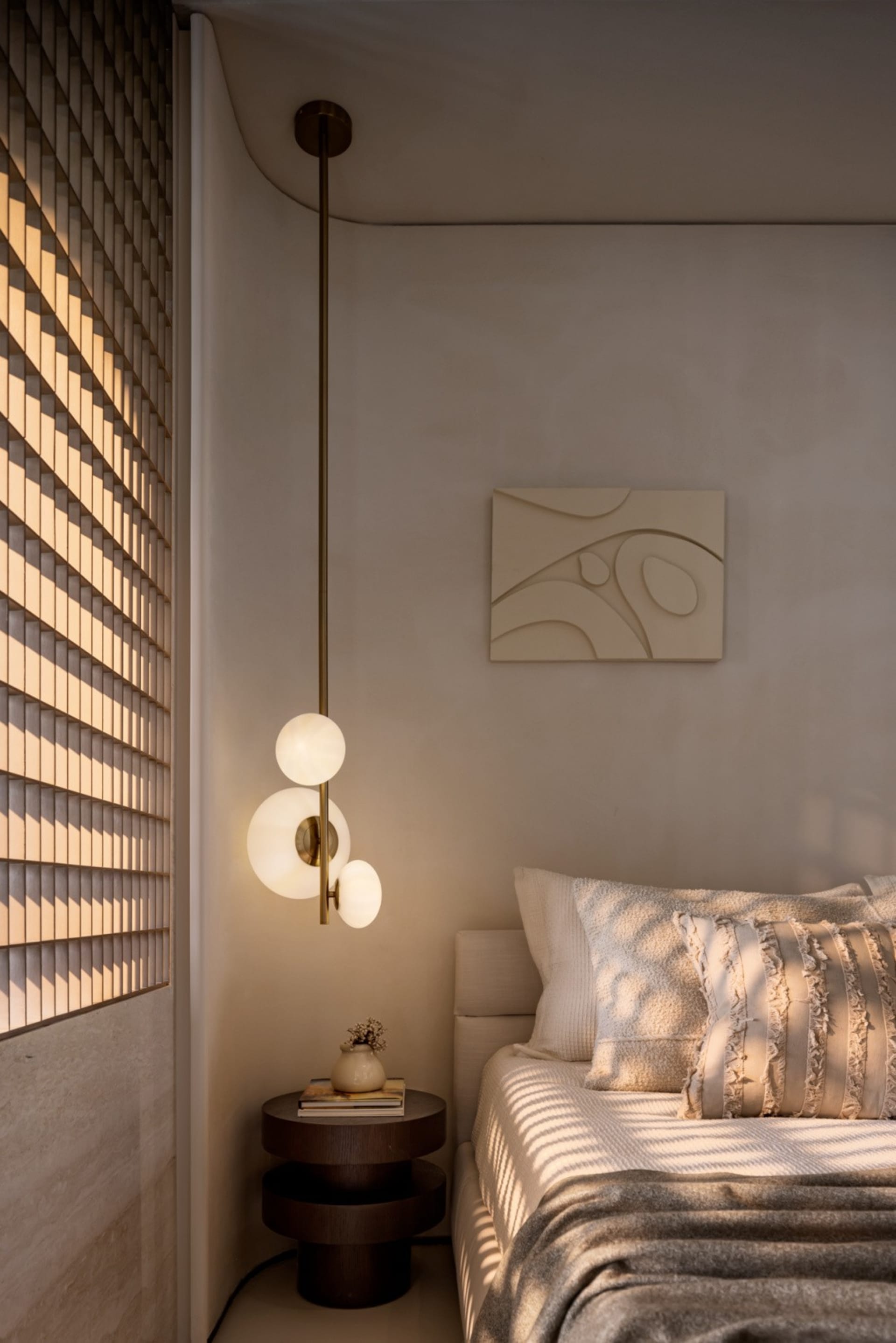 簡約臥室內有一張鋪著質感布料床罩的床，以及一盞懸掛式燈具。