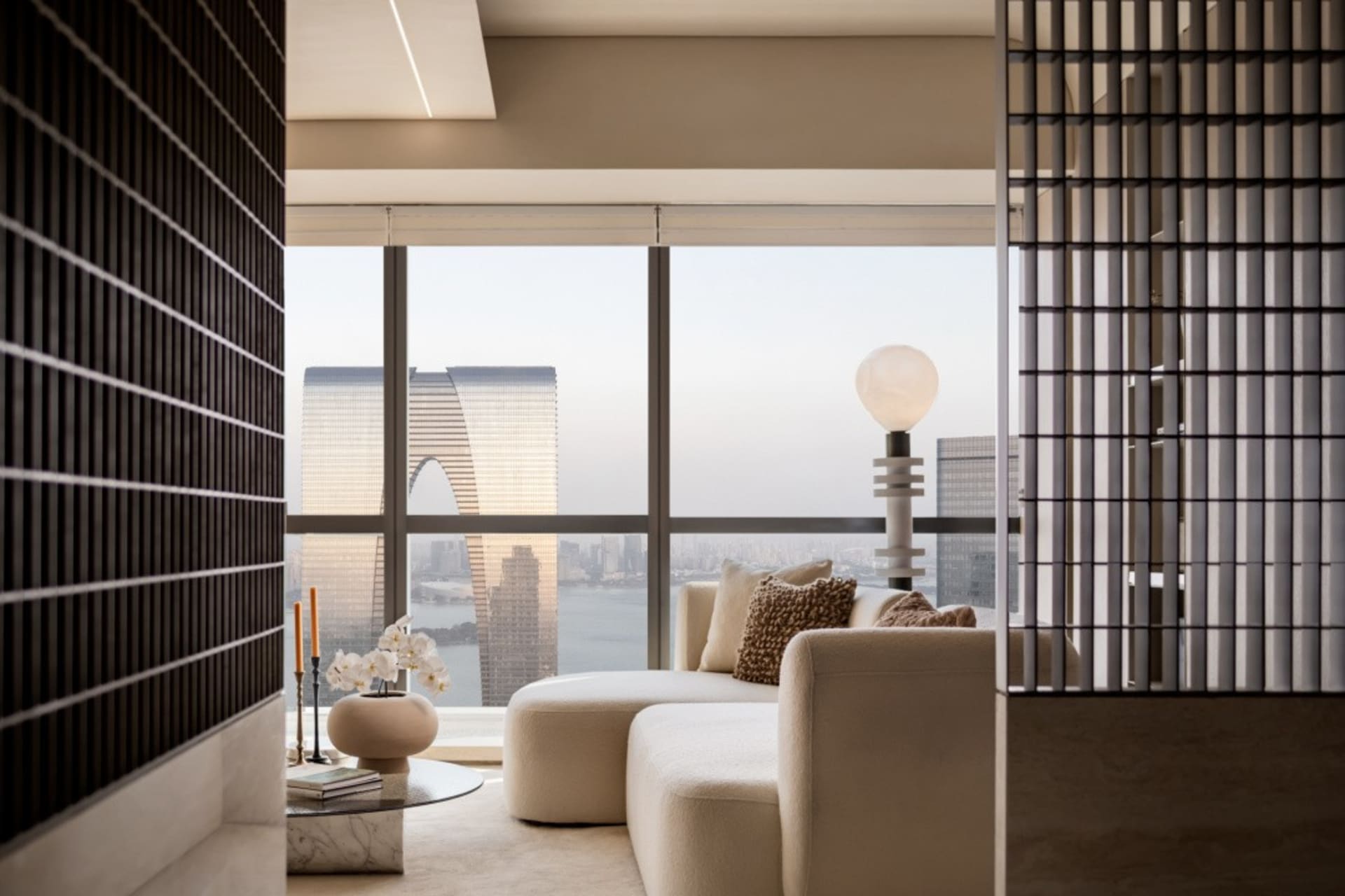 Modern living room with white furniture and glass windows overlooking a cityscape.