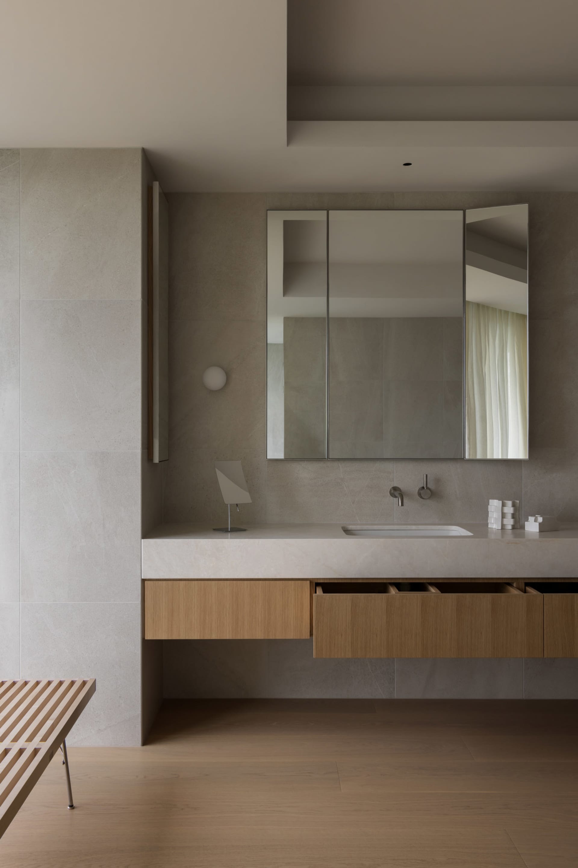 Modern minimalist bathroom featuring a floating wooden vanity with a white countertop, a large mirror, and a floating bench.