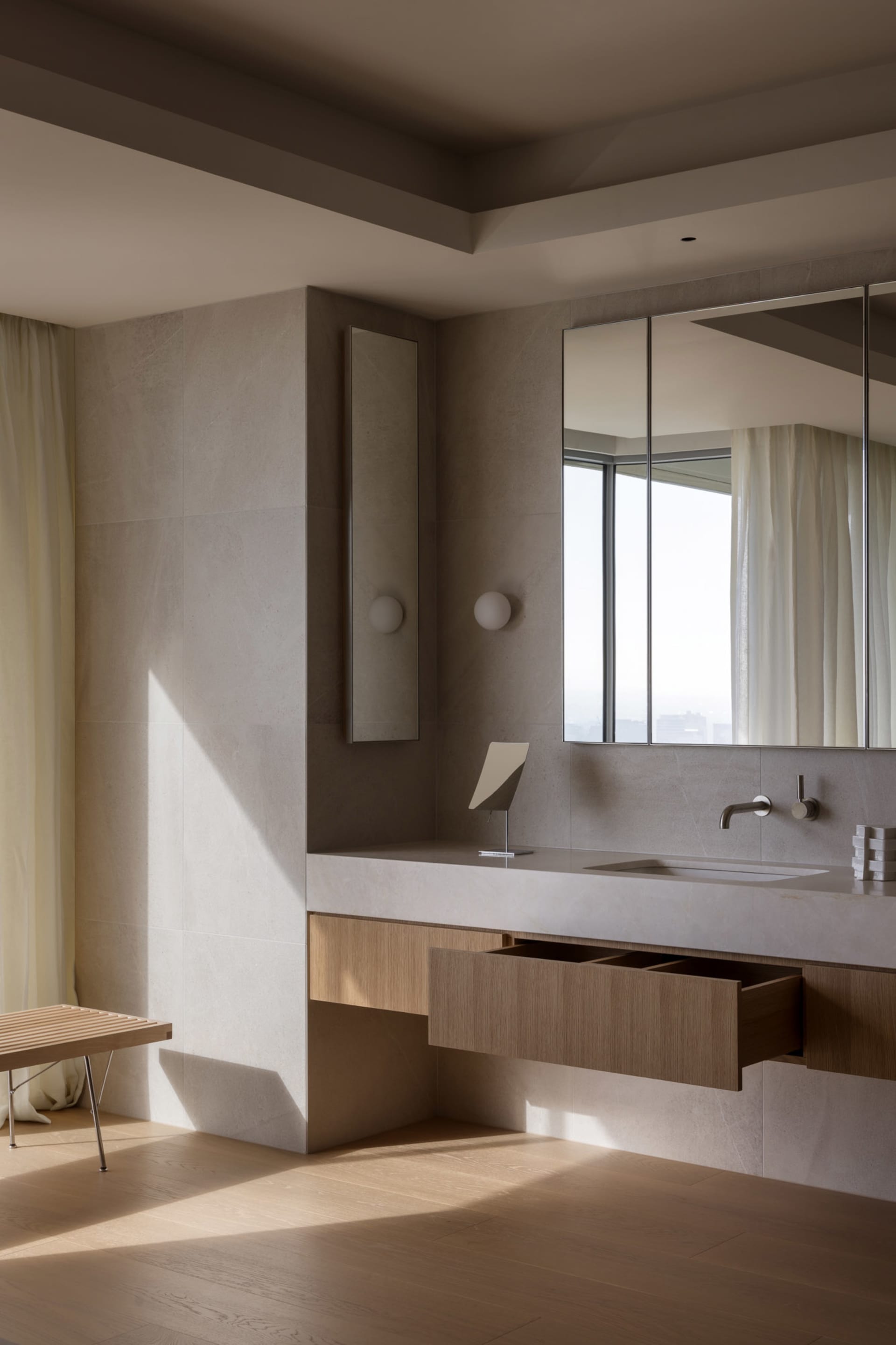 Modern minimalist bathroom featuring a white ceramic vanity, wooden drawers, and metallic fixtures against a textured ceramic