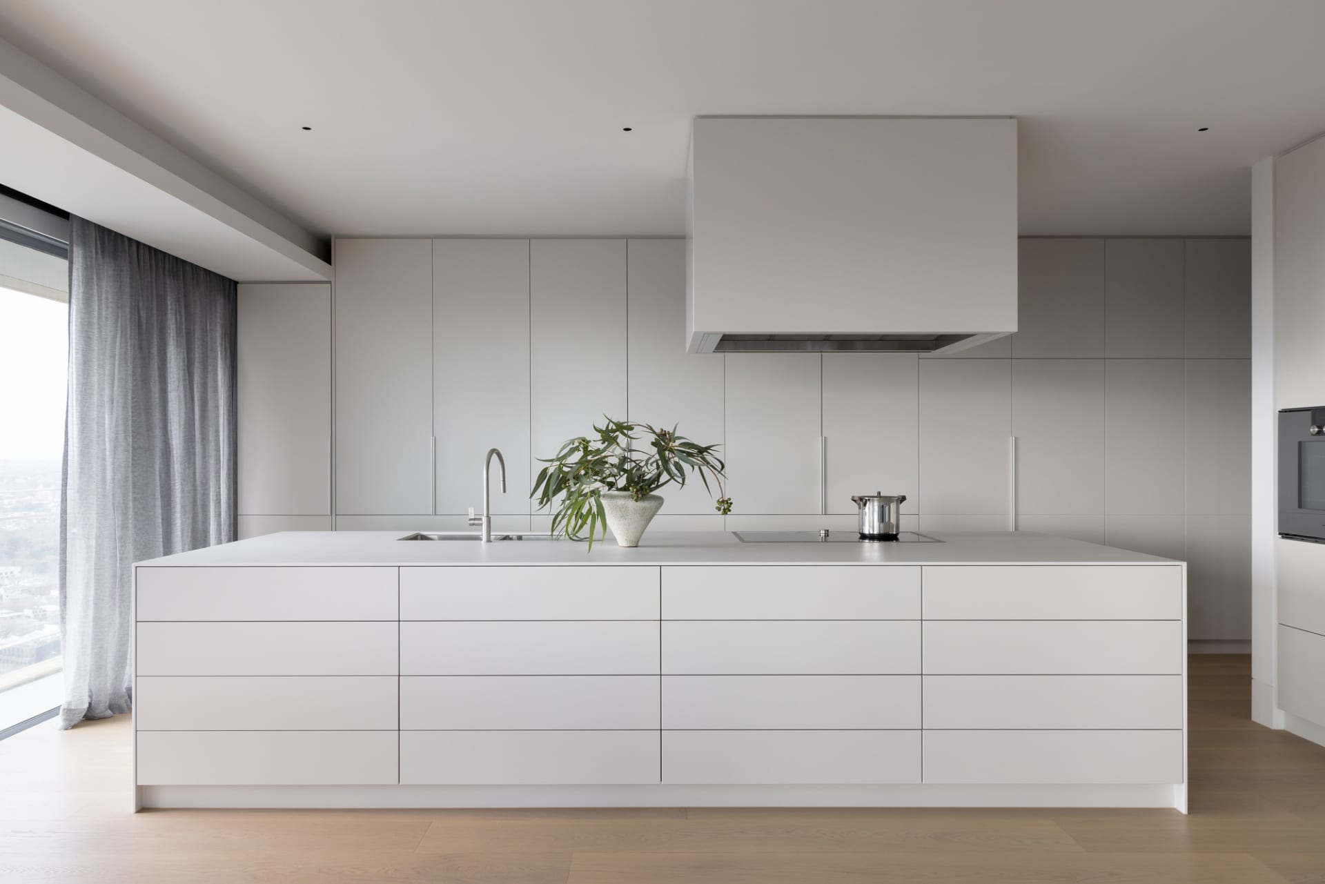 Modern minimalist kitchen with white cabinets, stainless steel appliances, and a large island.