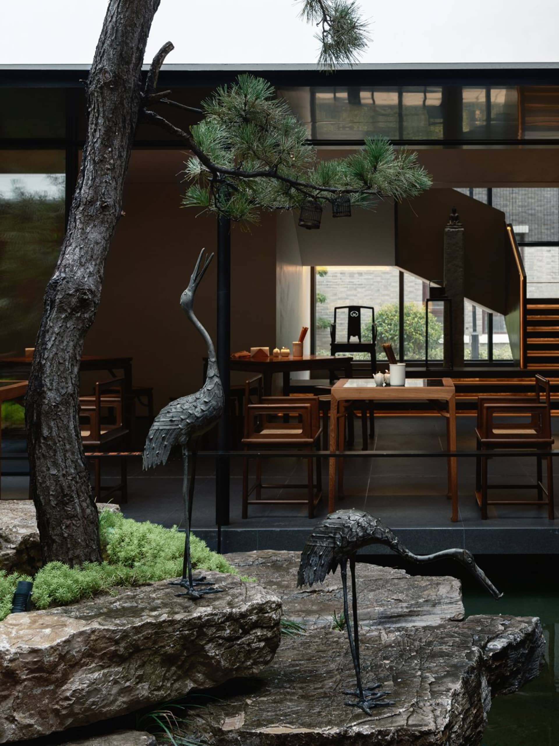 Modern restaurant interior with wooden tables, stone accents, metal sculptures, and glass features