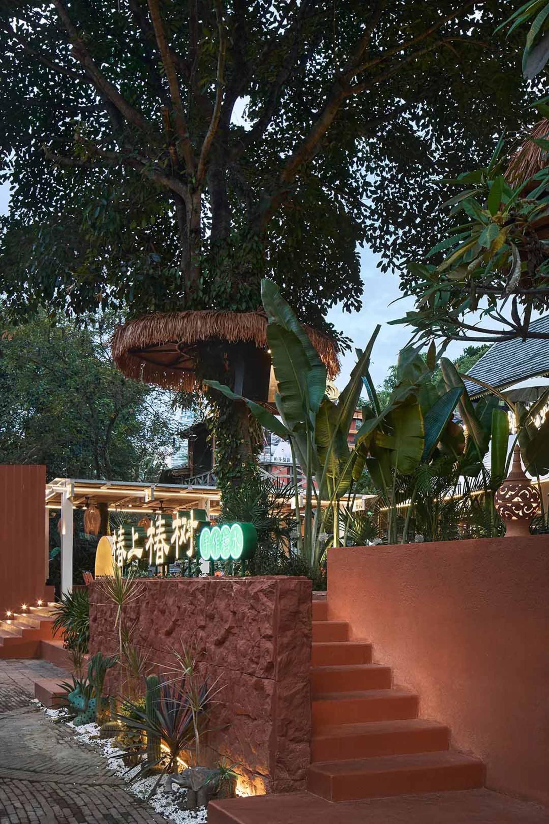A modern restaurant with brick stairs and tropical plants, featuring a treehouse-like structure.