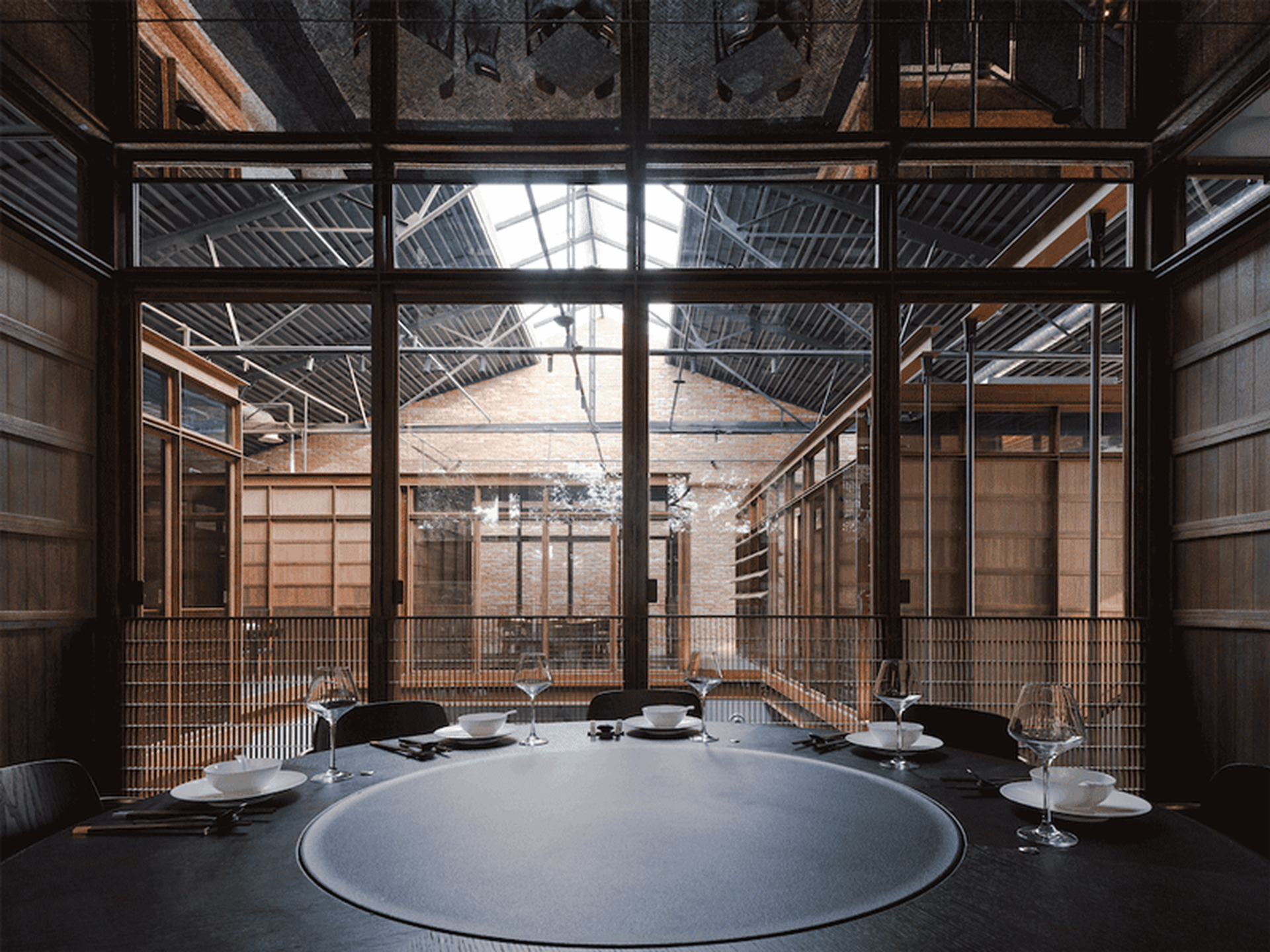 A round table in an industrial restaurant space with wooden walls, glass windows, and metal railings.