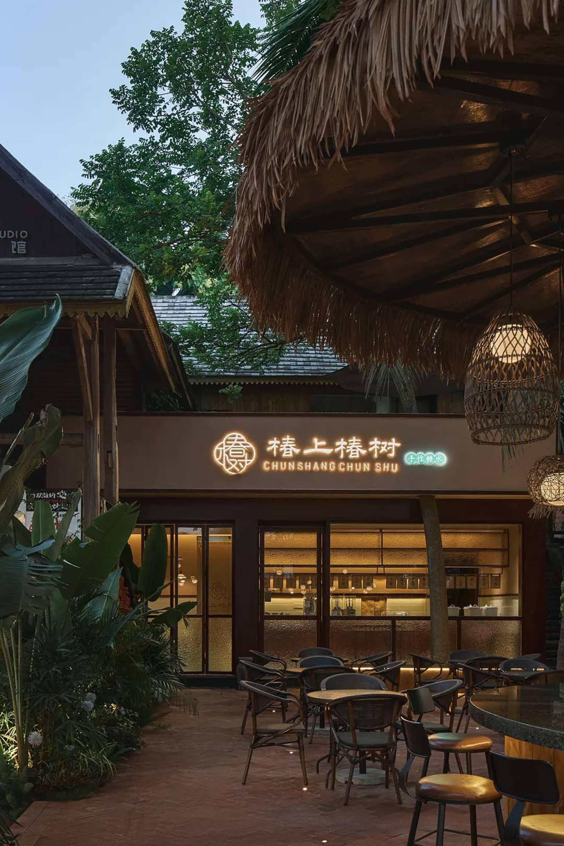 A restaurant with a wooden roof and tropical design elements, featuring chairs and tables under a thatched umbrella.