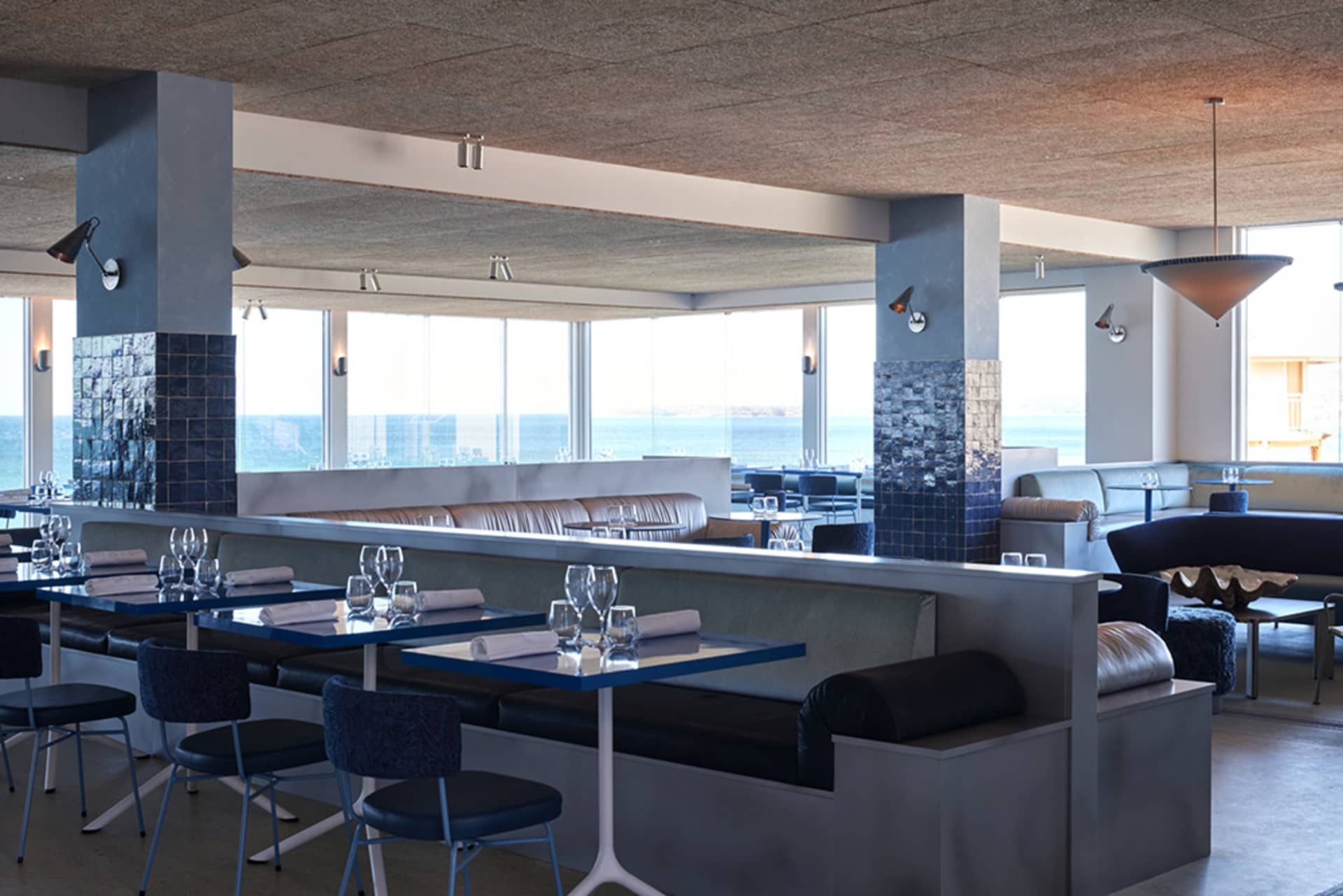 Modern restaurant interior with concrete walls, glass windows, and leather seating