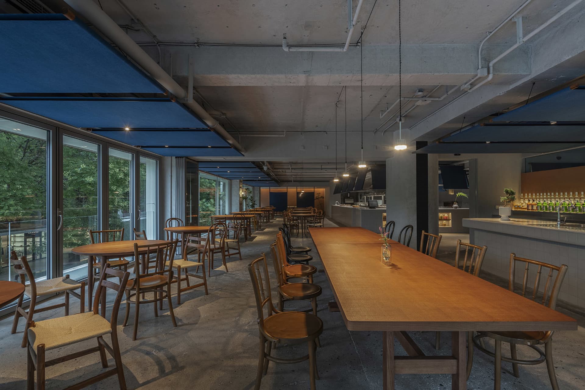 工業風餐廳室內,搭配木質桌椅、混凝土天花板與大面窗戶。