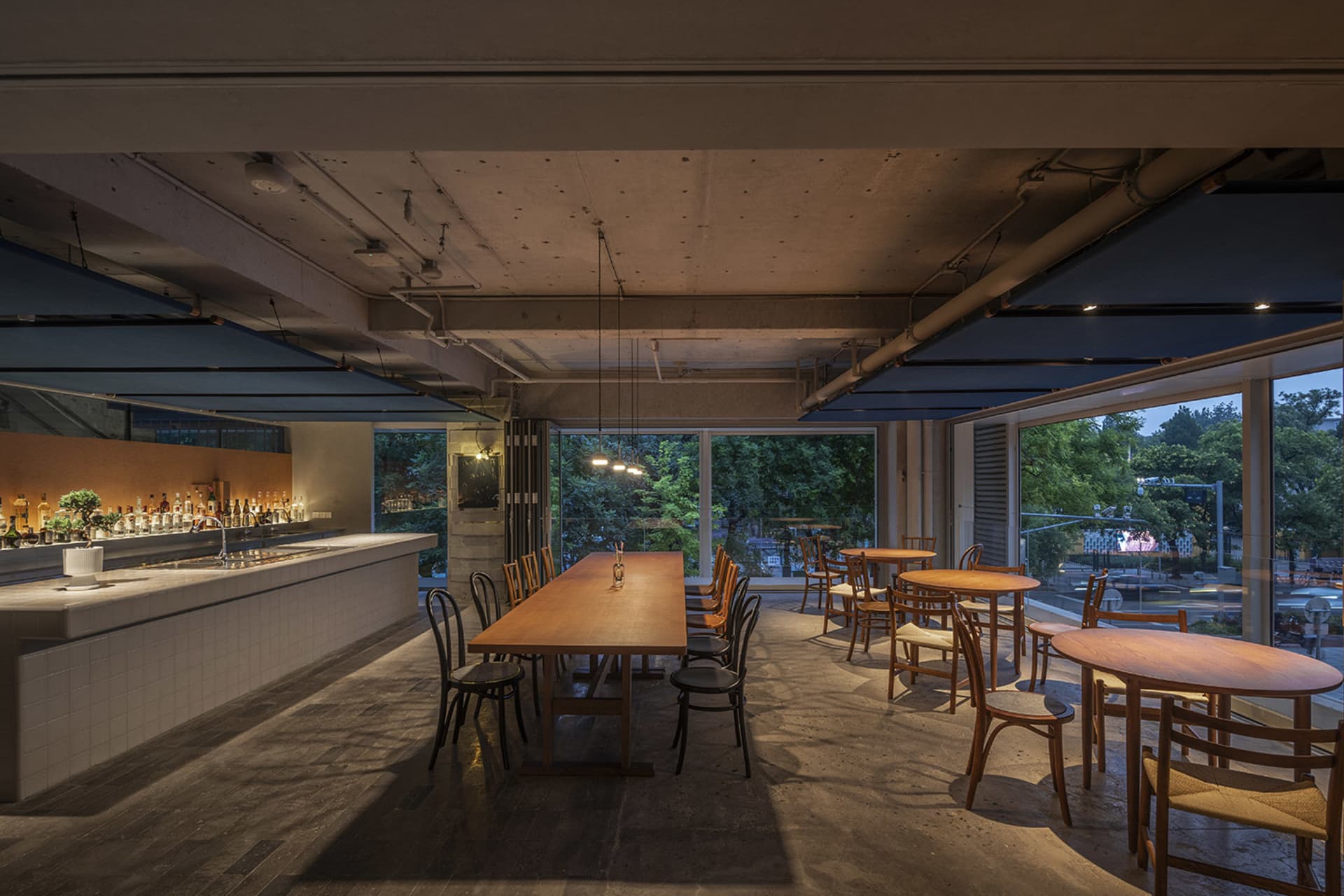 A modern restaurant interior featuring wooden tables, concrete flooring, and glass elements.