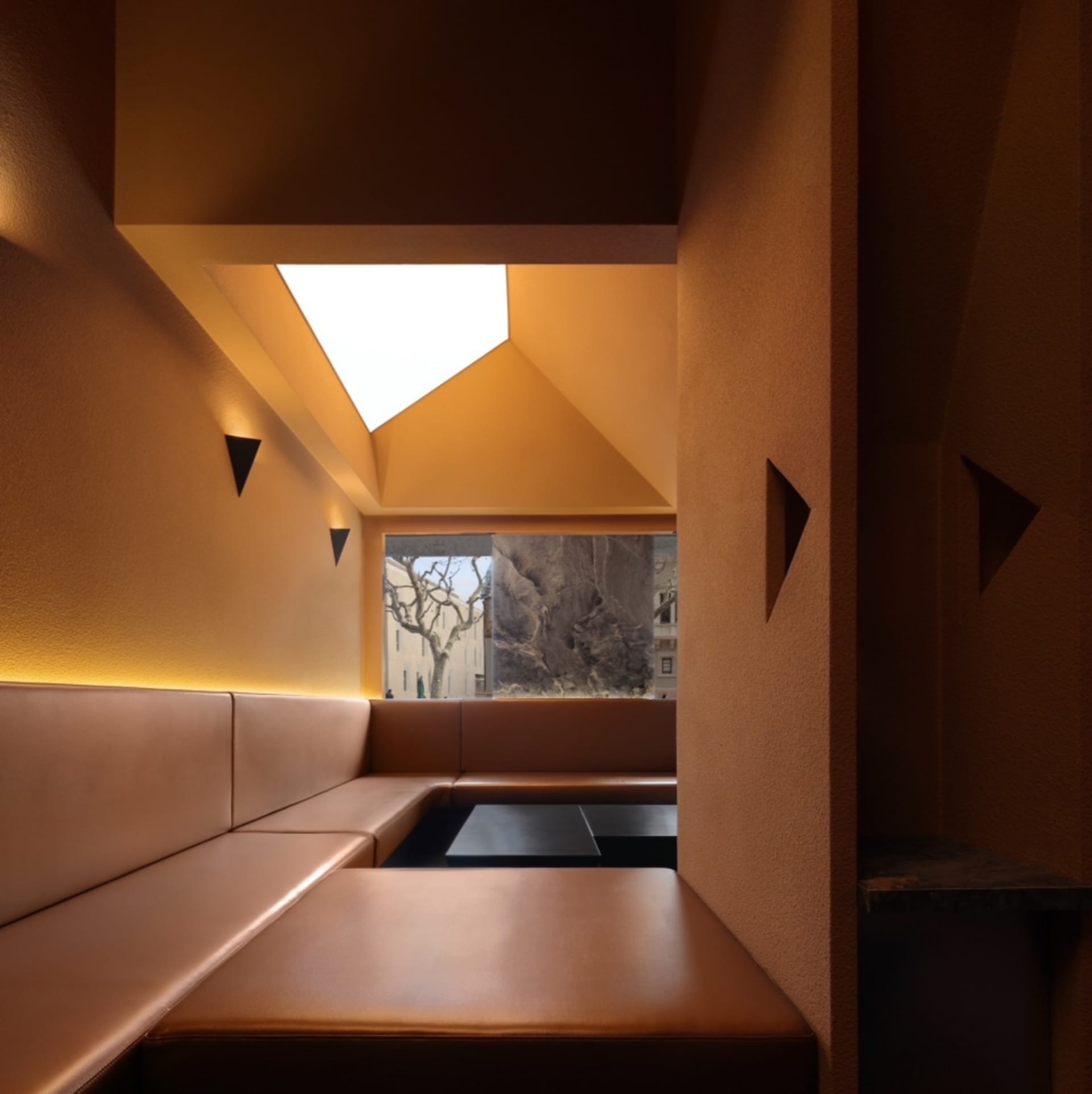 Leather booths in modern restaurant setting, illuminated by warm lighting from a skylight.