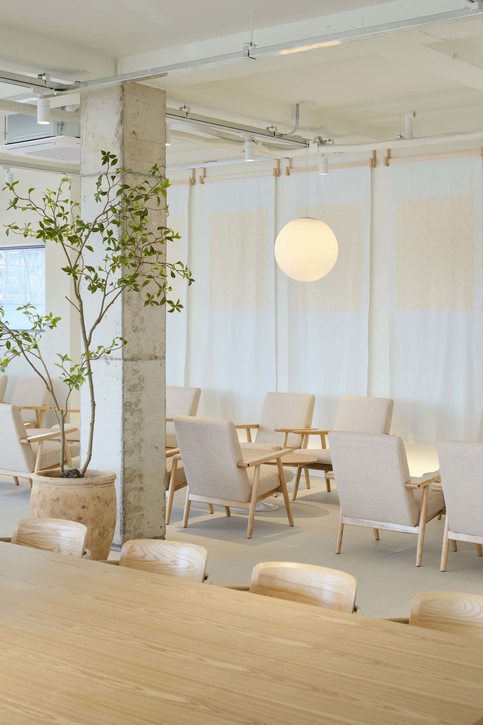 A minimalist coffee shop with concrete walls, wooden furniture, and white fabric seating.