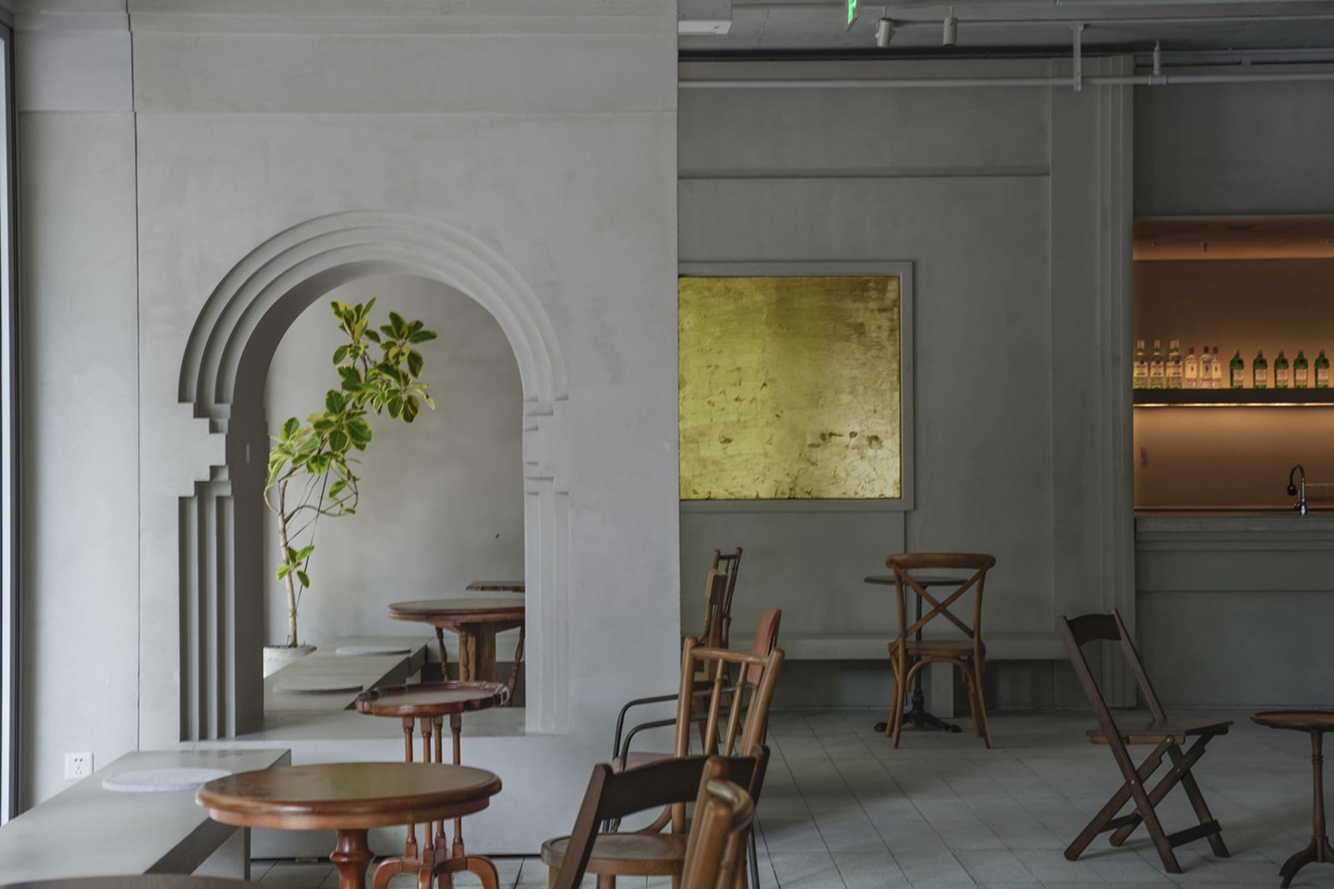 A modern cafe interior featuring a concrete wall with an arch and a gold-framed wall art.