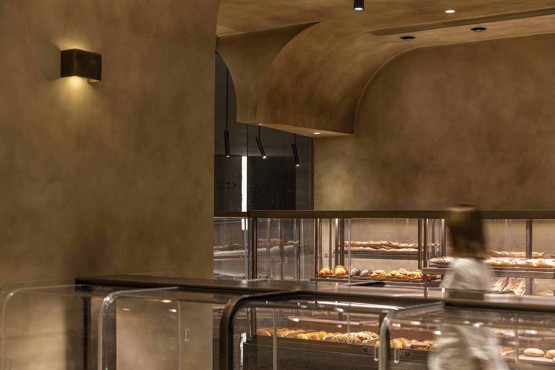 Modern bakery interior with metallic finishes and illuminated bread display cases.