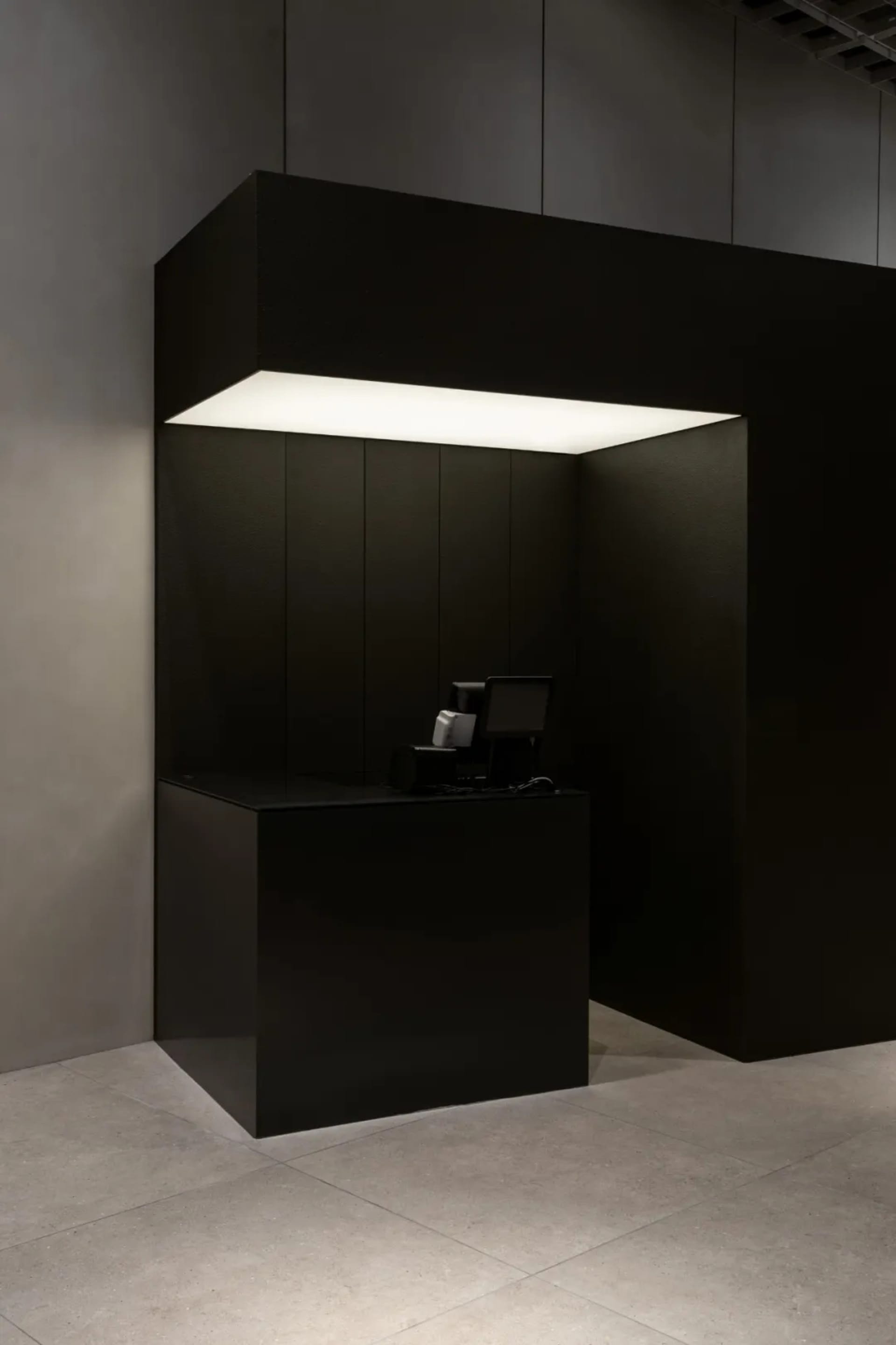 A minimalist black reception counter with a metallic finish, illuminated by a sleek overhead light fixture.