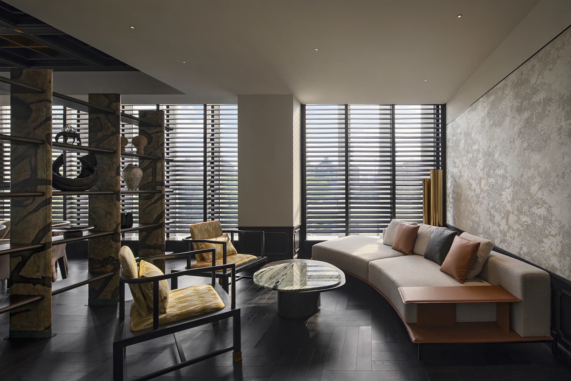 Modern living room with a curved sofa, armchairs, and a coffee table in a neutral-toned material setting.