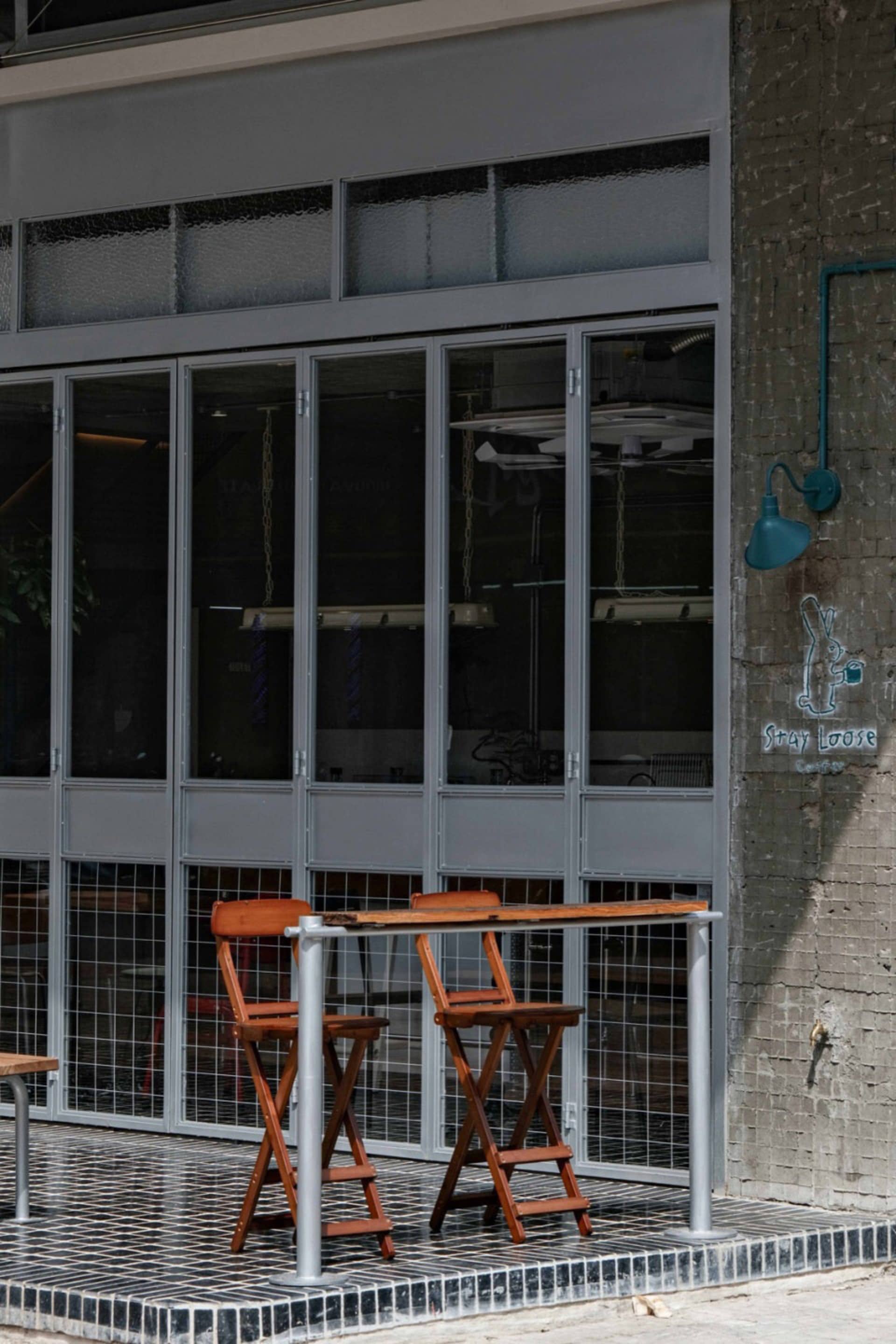 Outdoor seating area of a street cafe featuring industrial design elements like wood furniture, metal railings, and large gla