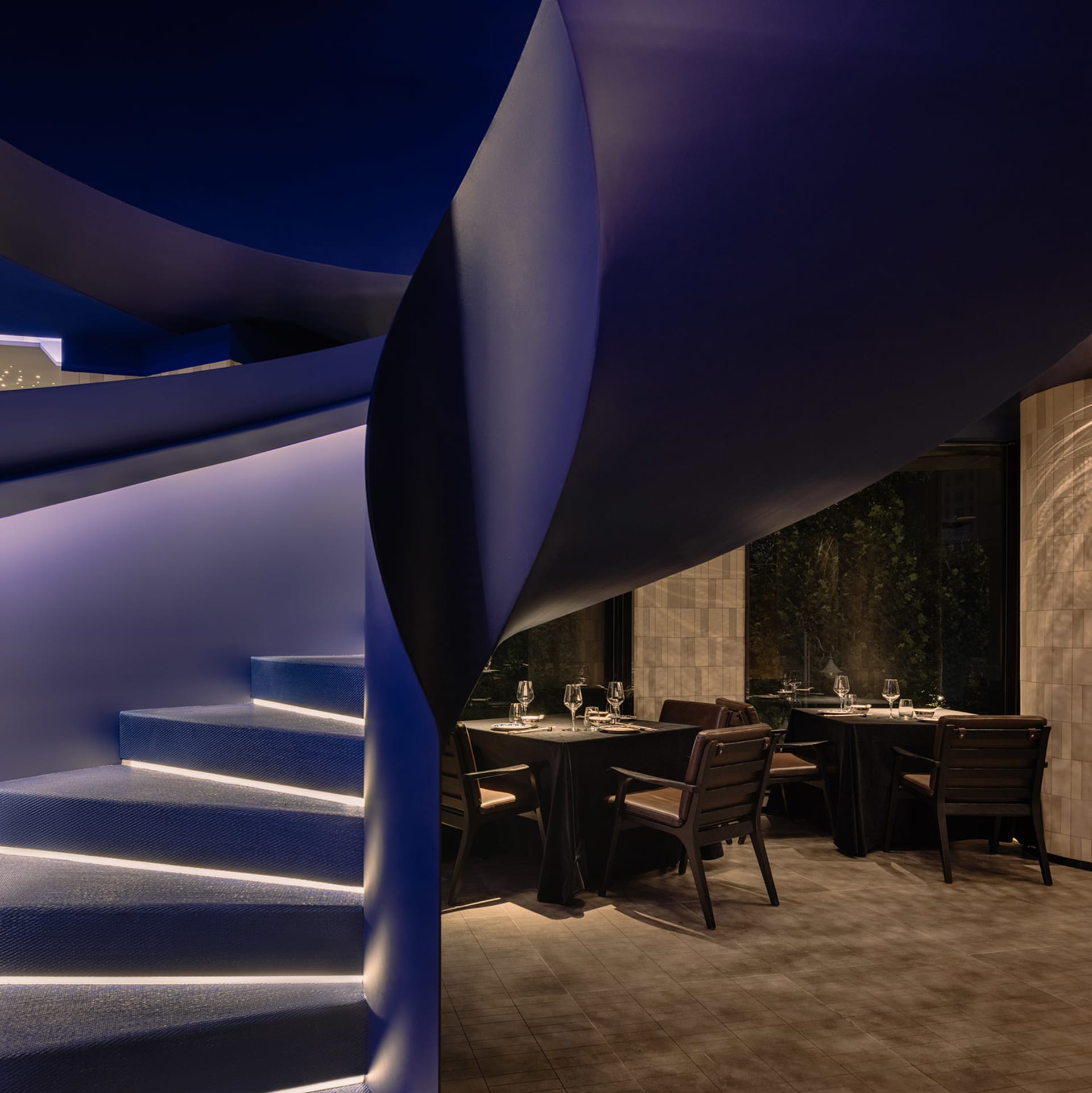 A modern restaurant interior featuring a curved, illuminated blue staircase.