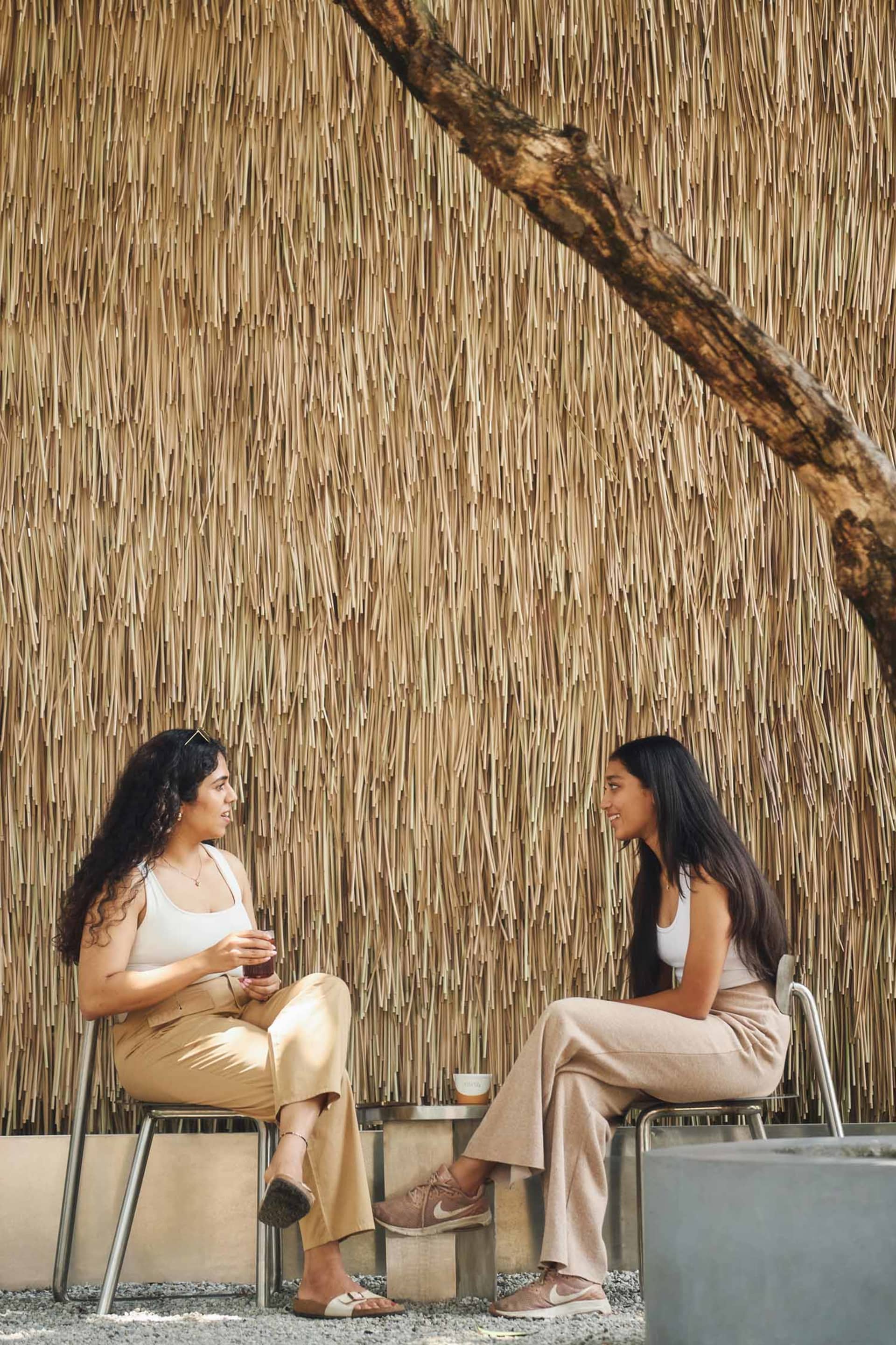 Two women having a conversation in a space adorned with reeds