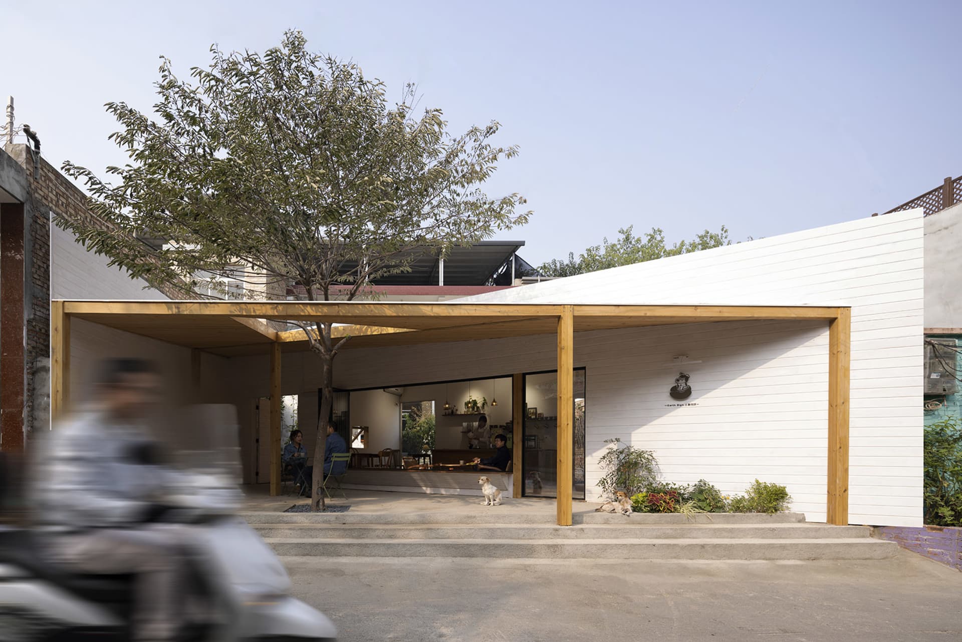 A minimalist restaurant exterior with white paneled walls and a wooden canopy.