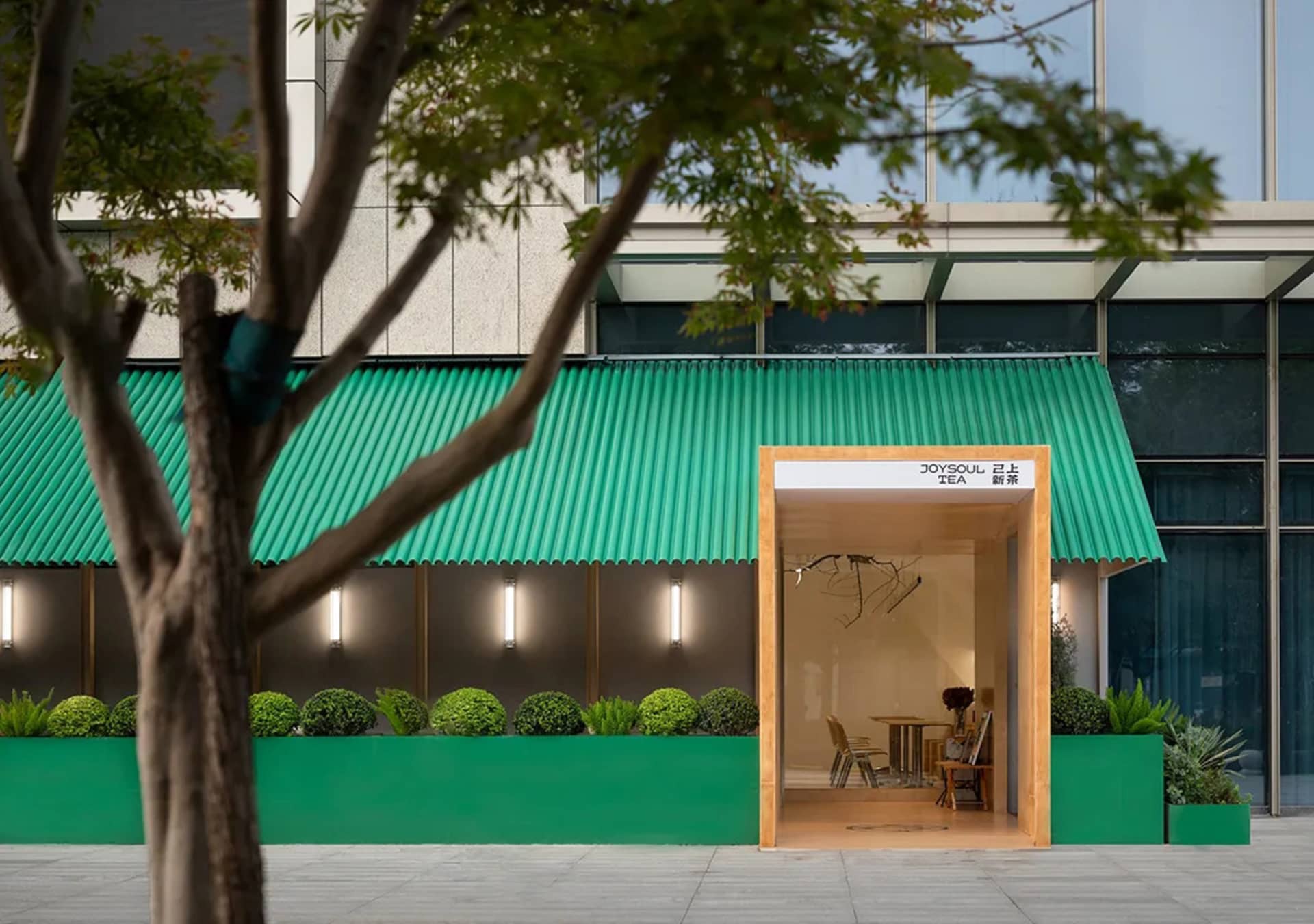 A modern coffee shop exterior with green metal cladding and a tree in the foreground.