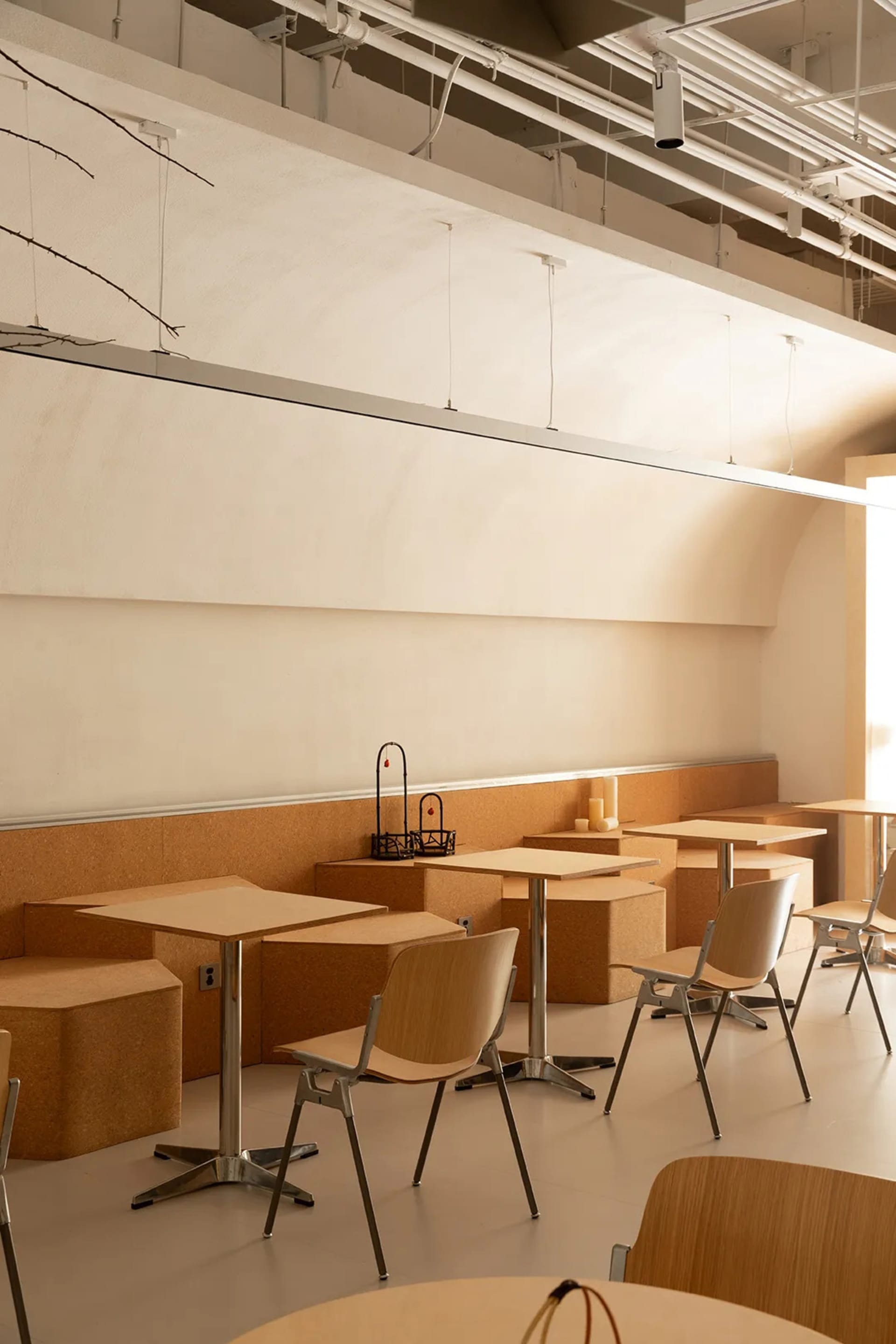 Modern cafeteria with minimalist design featuring wooden and cork tables and chairs.