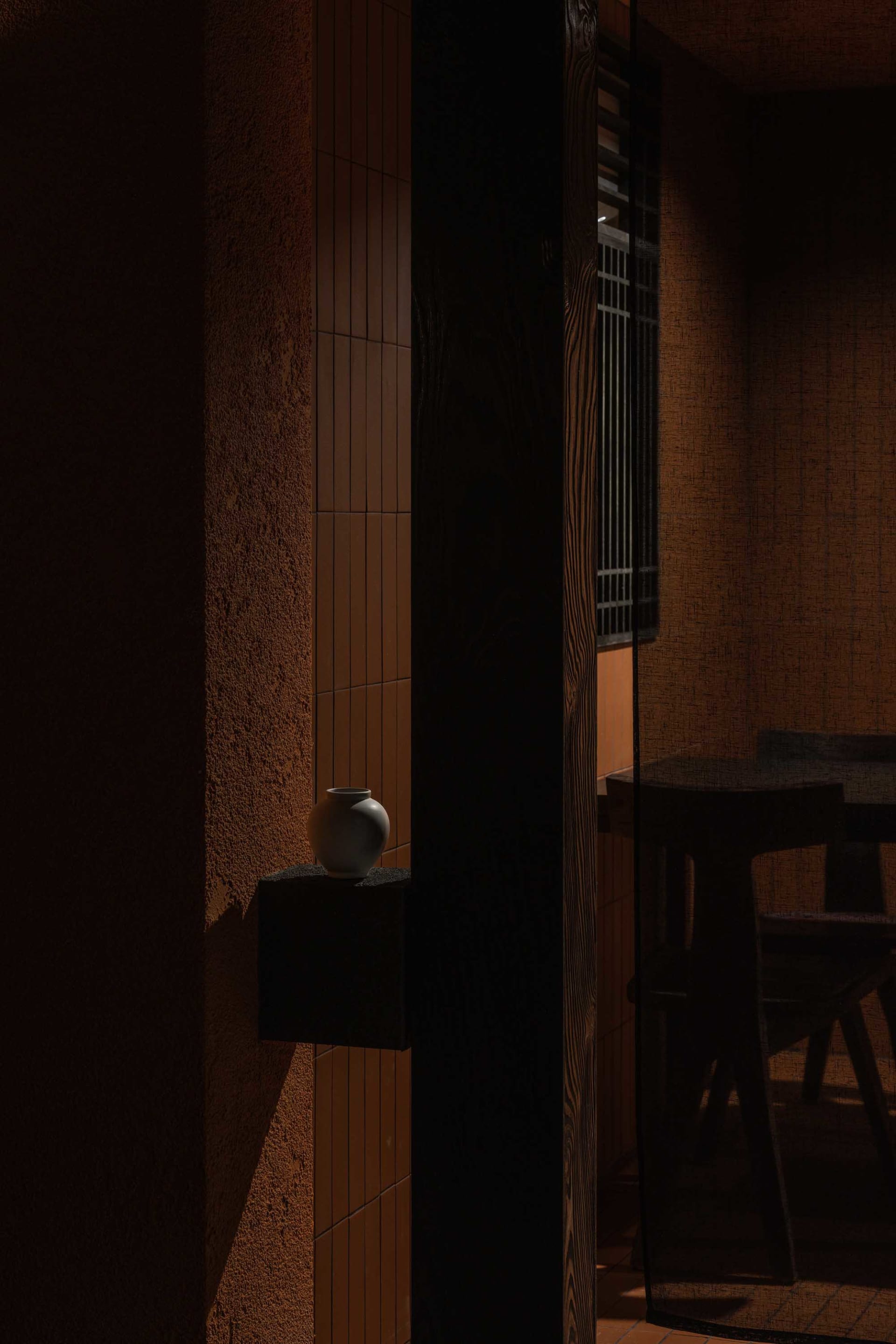 A dark interior setting featuring a ceramic vase on a shelf.