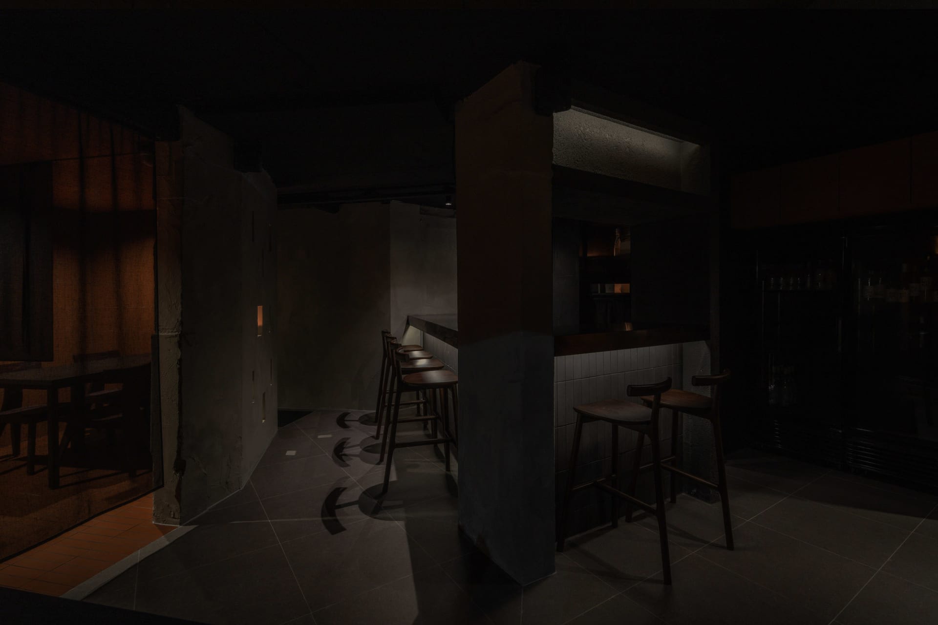 A minimalist bar interior featuring wooden stools, concrete walls, and metallic accents.