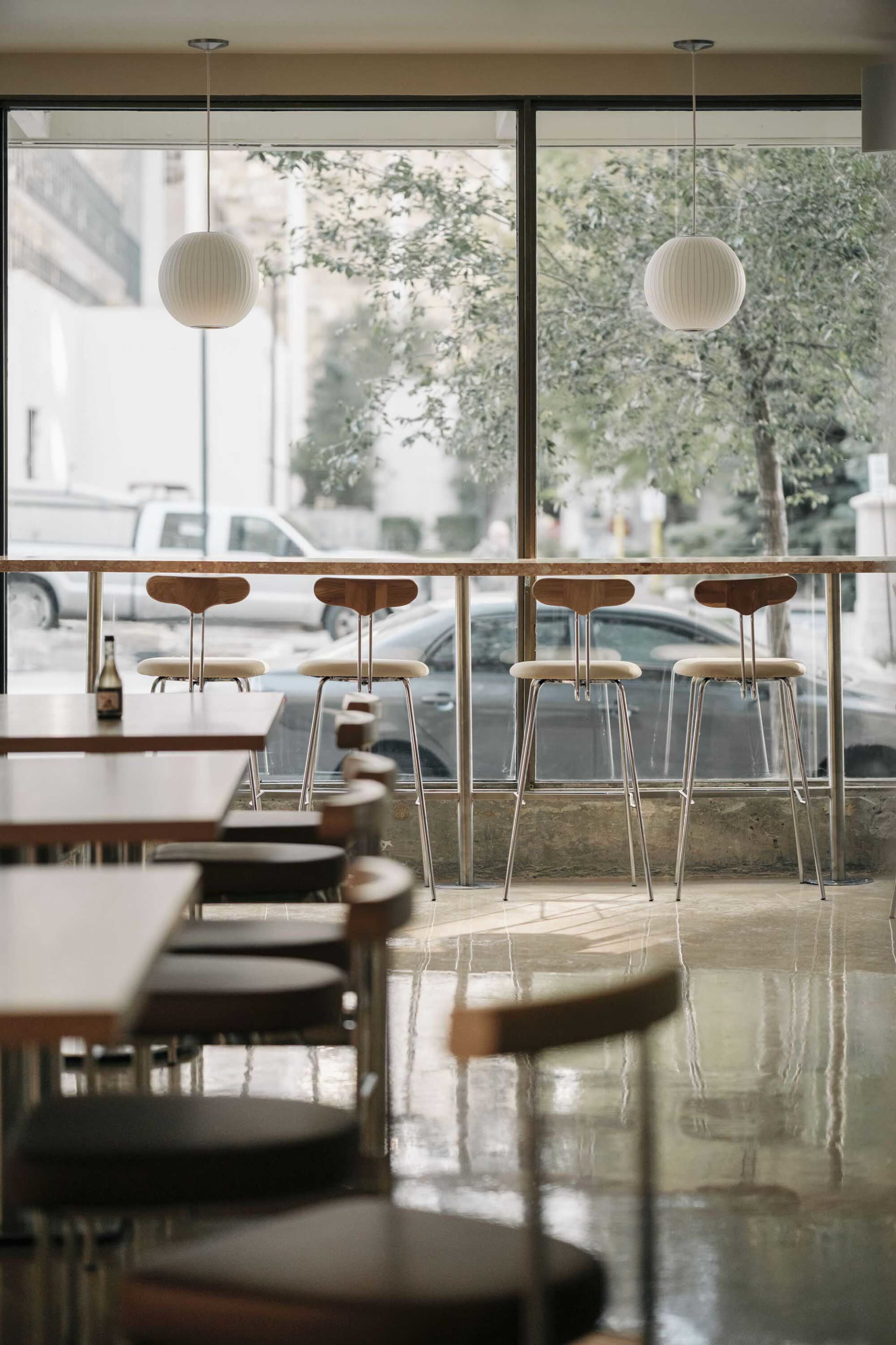 A modern restaurant bar area featuring white pendant lights, teak bar stools, and a sleek counter.