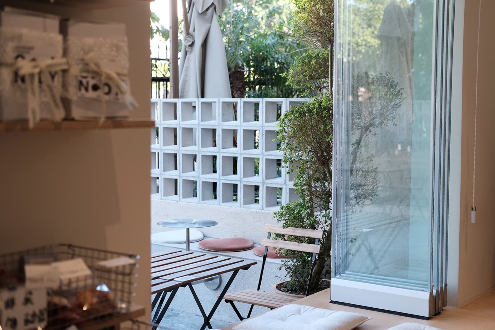 A modern cafe outdoor terrace featuring concrete blocks, glass walls, and wooden furniture.