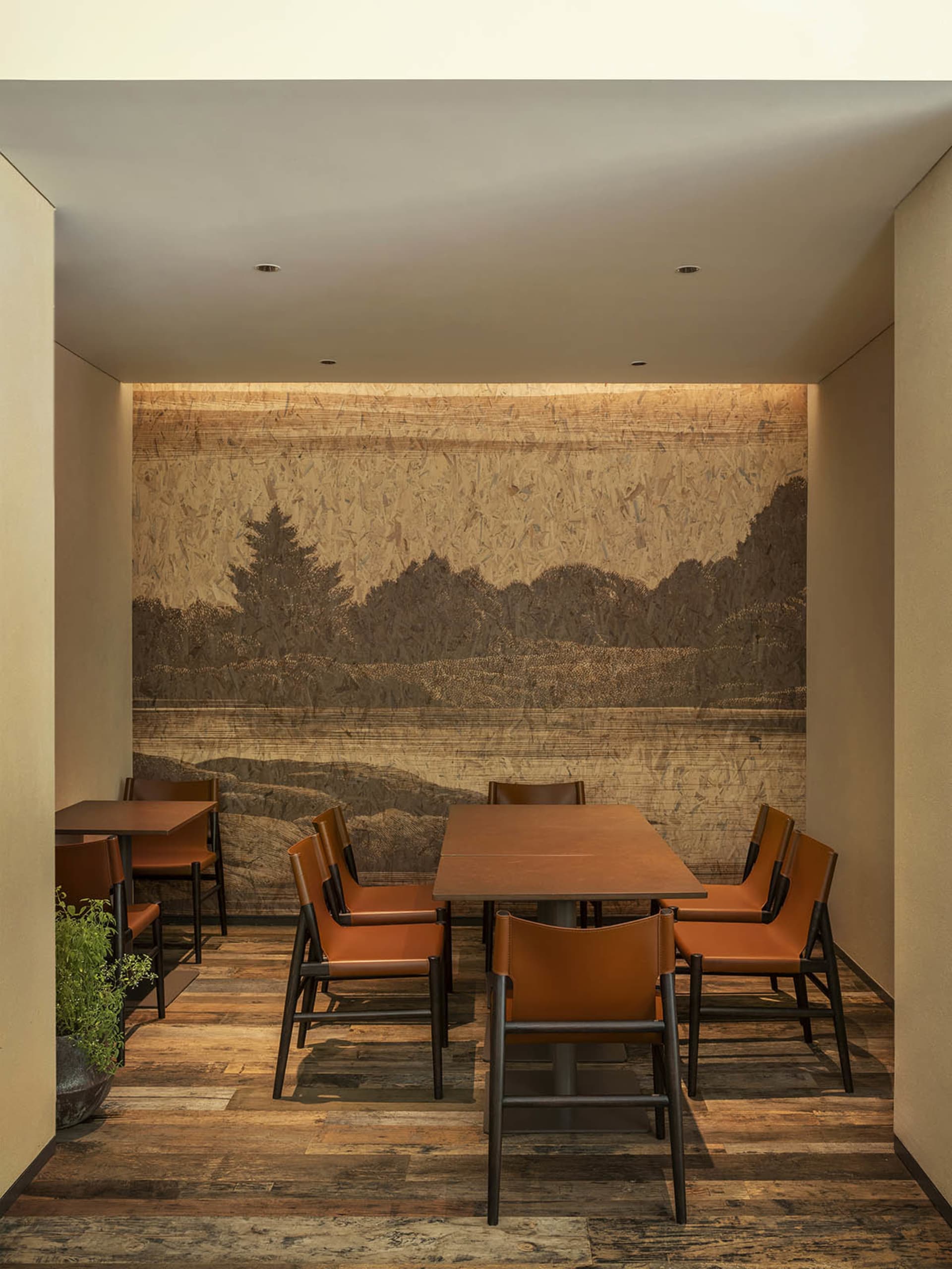 A modern restaurant interior featuring wooden tables and chairs with leather upholstery, a scenic mural on the wall depicting