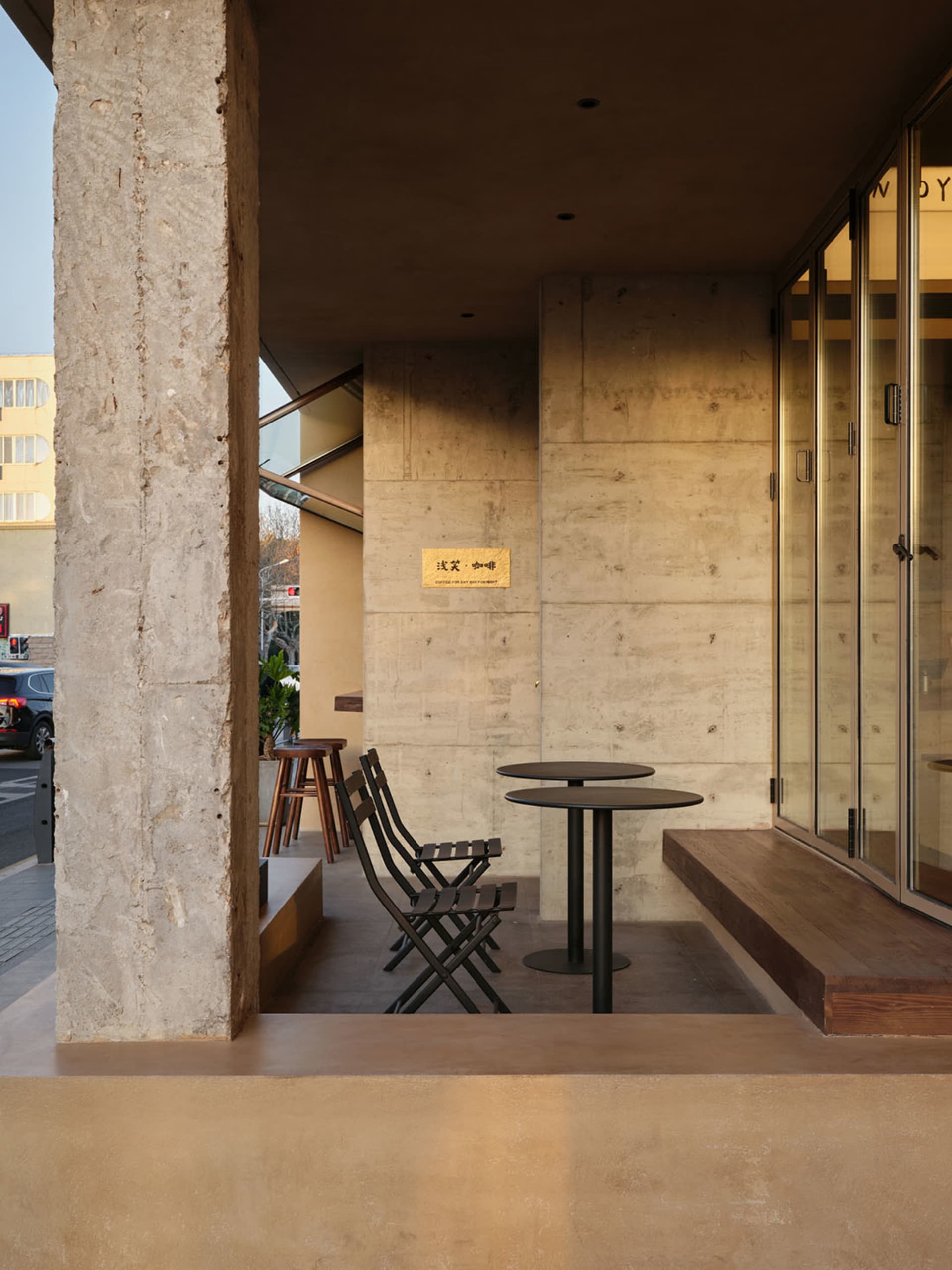 A modern cafe exterior with a concrete facade, featuring tables and chairs.