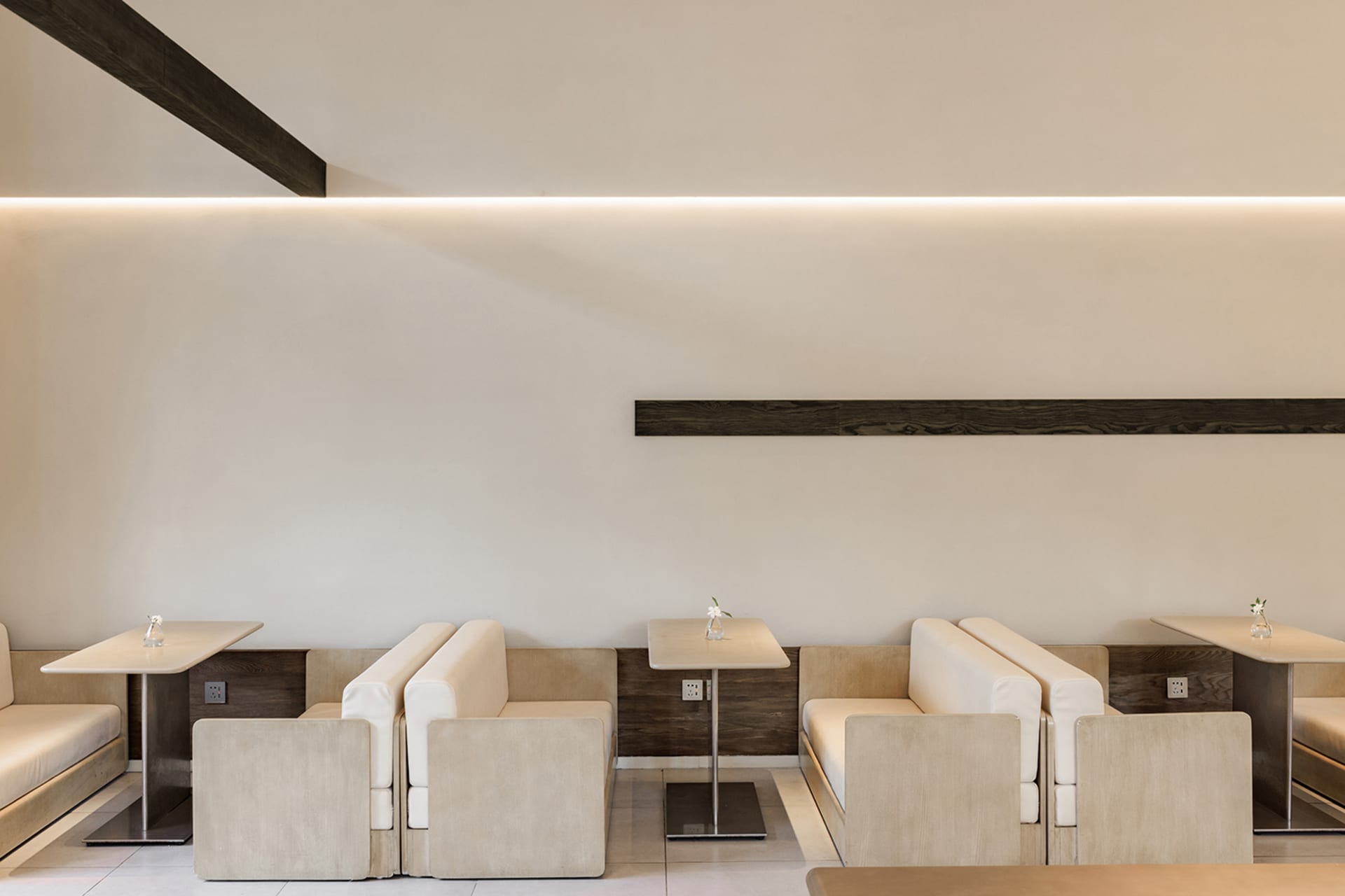 A modern minimalist restaurant featuring beige fabric seating and dark wooden accents.