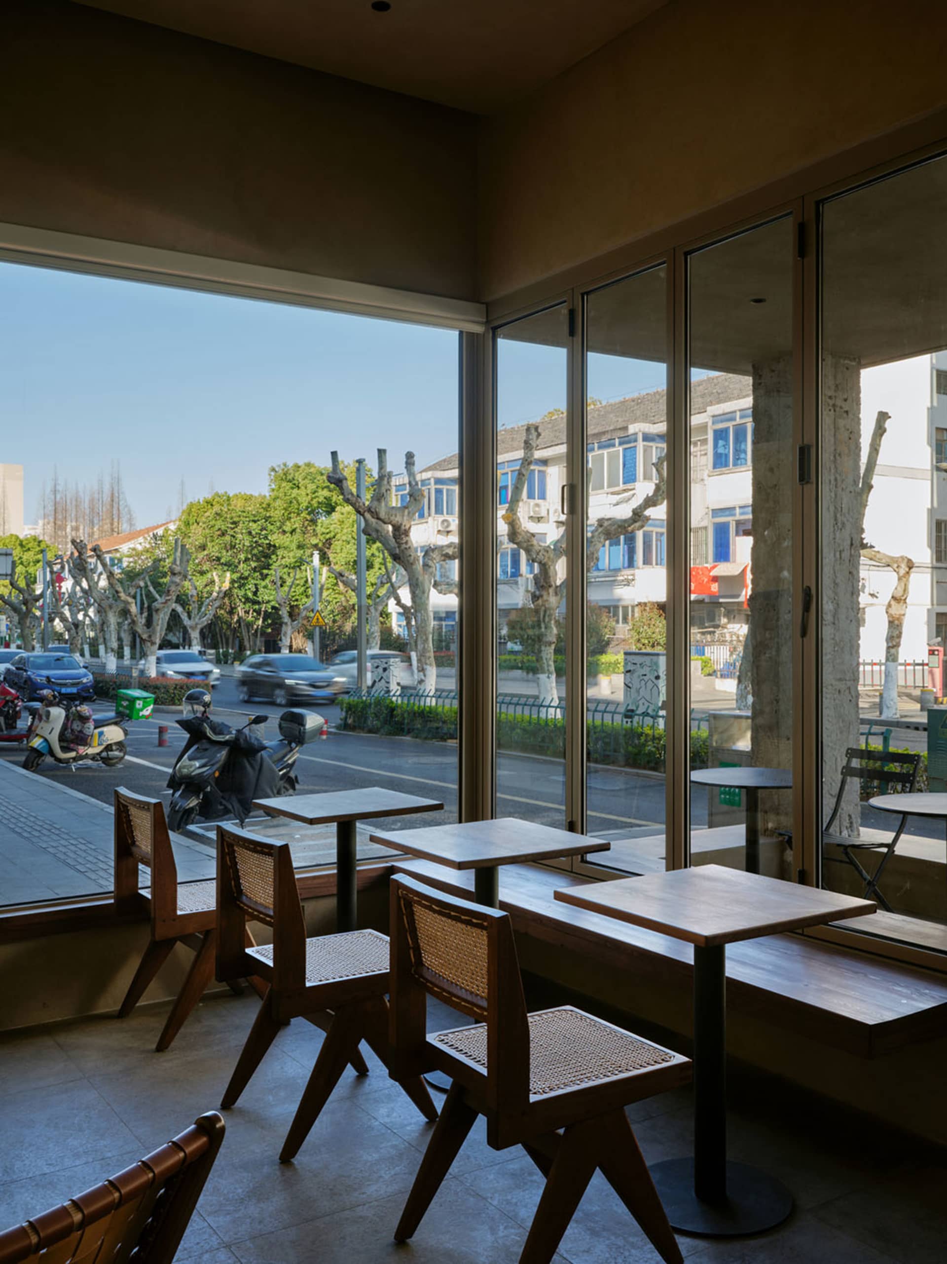 咖啡廳室內擺放木質餐桌，搭配玻璃牆面，可眺望街景。