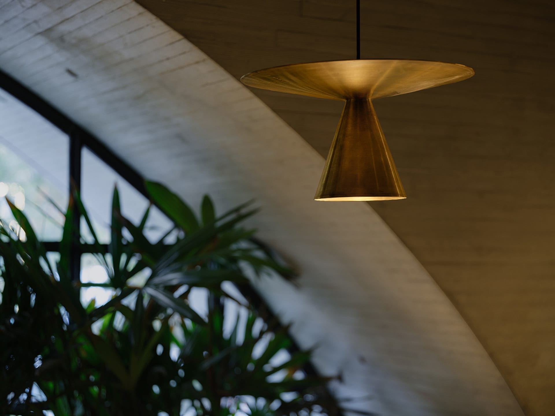 A modern living room featuring a brass pendant lamp hanging from a concrete ceiling.