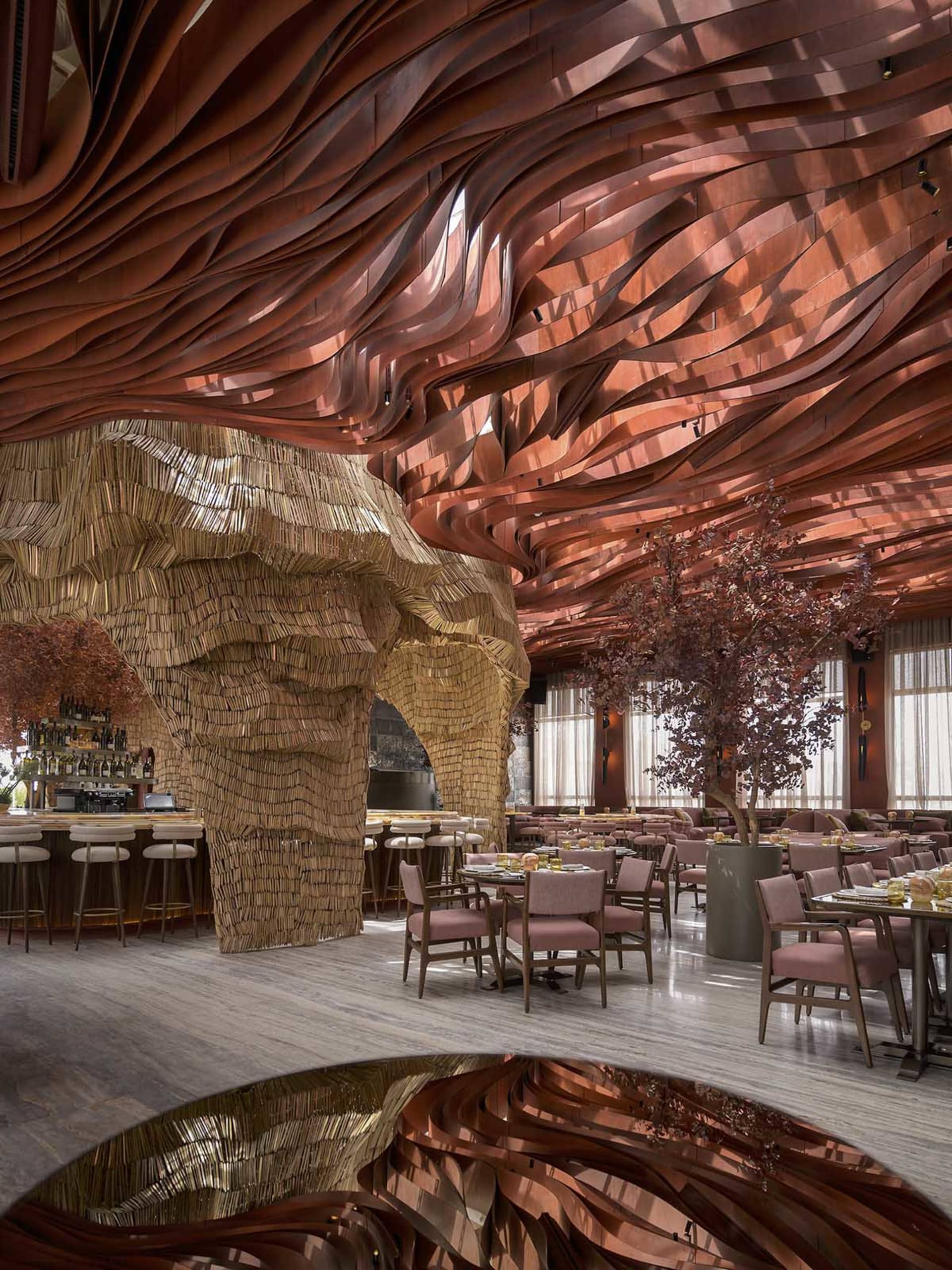 A contemporary restaurant interior featuring a wave-like, wood-textured ceiling and a bar area with stools.