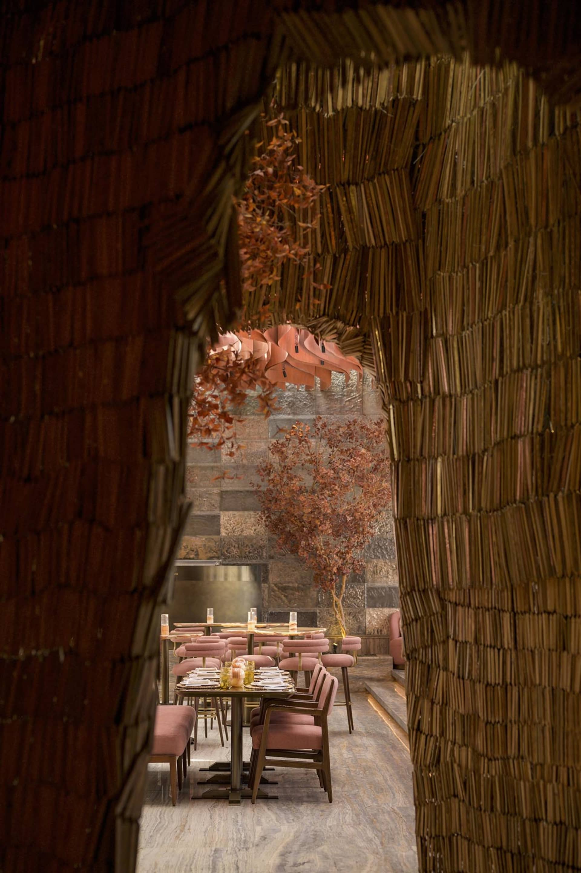 A cozy restaurant interior with tables set for service, surrounded by natural materials like thatch and wood.