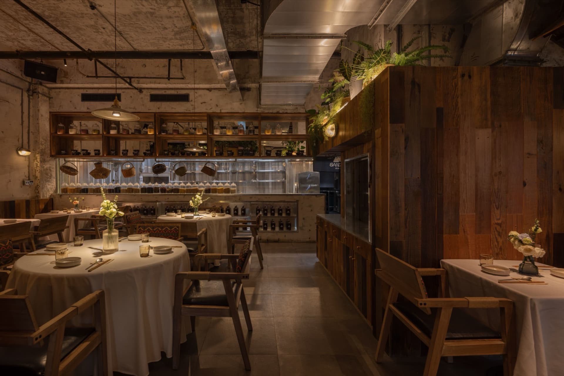 A warm, industrial-themed restaurant interior with wooden furniture, concrete accents, and greenery.