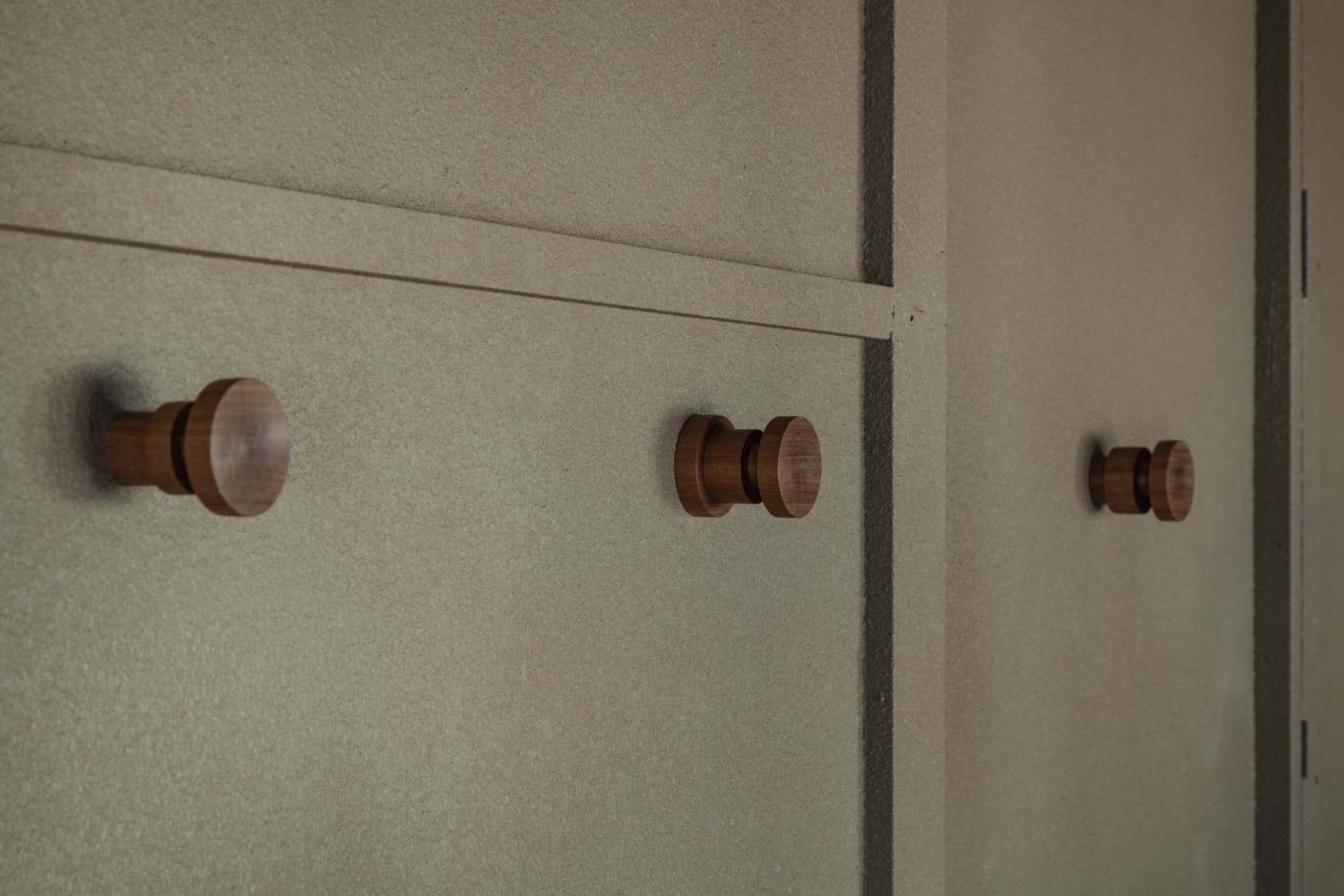 Minimalist design of wooden handles on a smooth, neutral-colored wall.