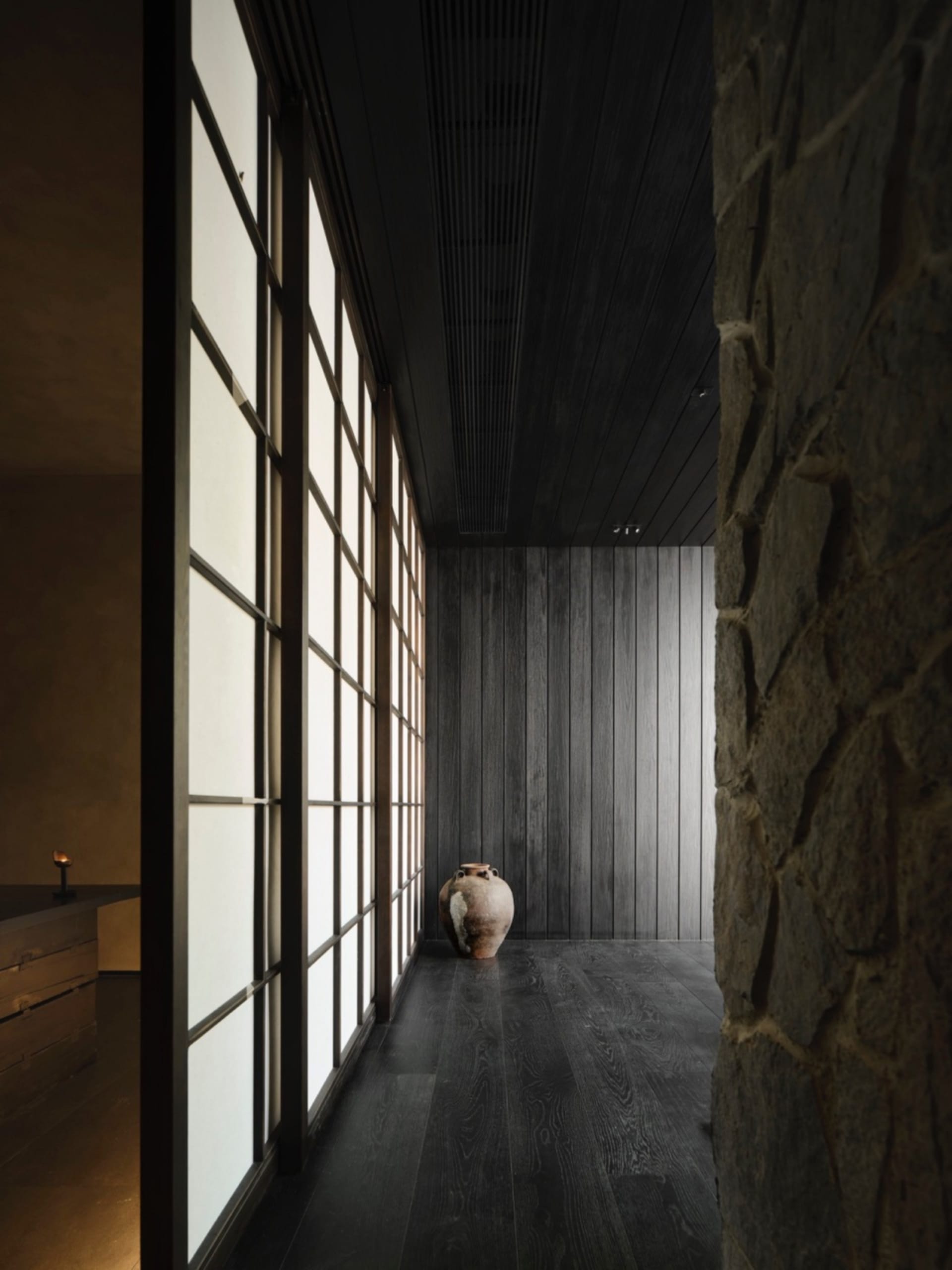 A minimalist modern interior space featuring wood paneling and traditional Japanese shoji screens, with a vase on the floor.