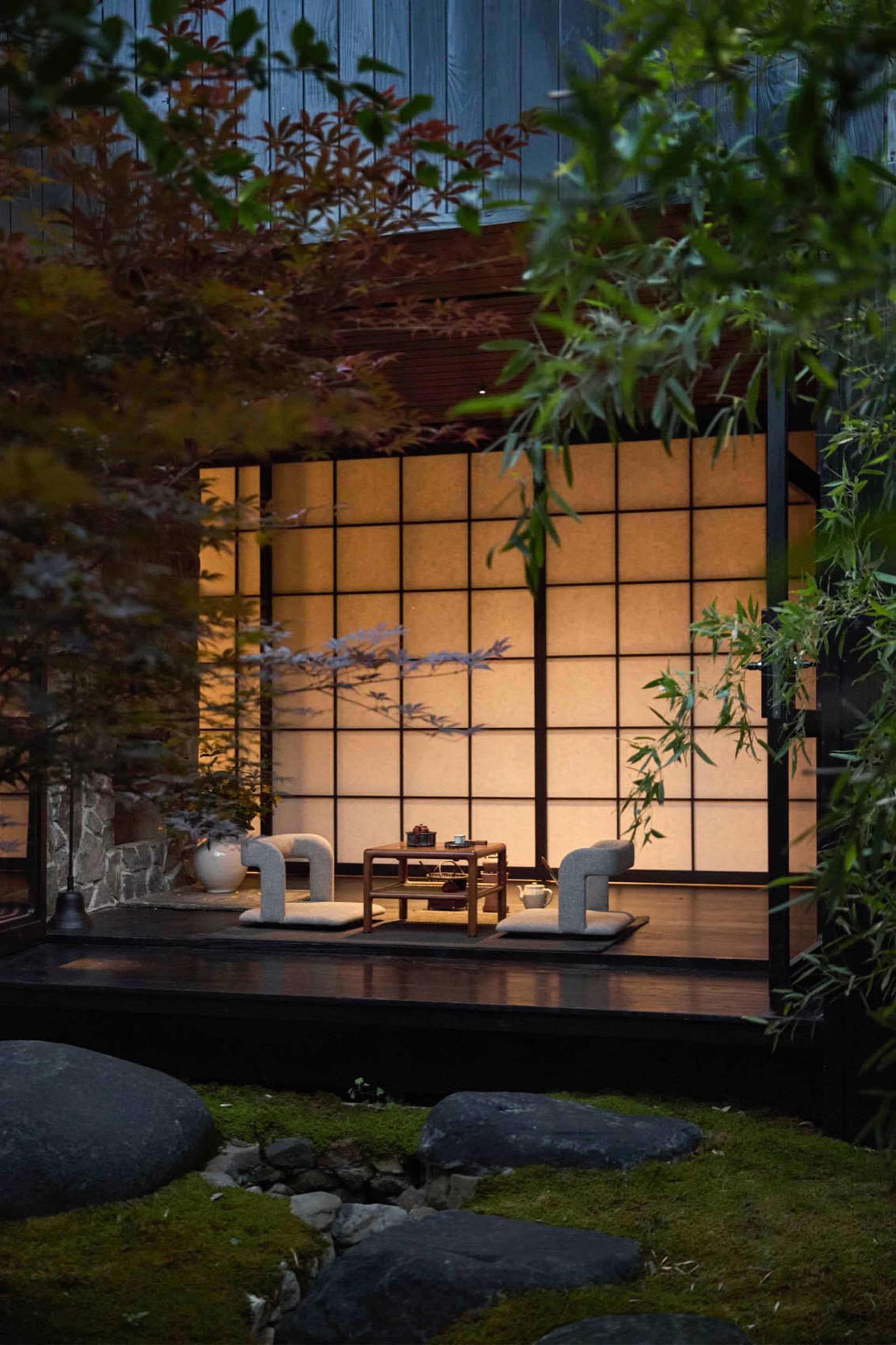 A serene Japanese tea terrace with seating and a table, surrounded by stone and greenery.