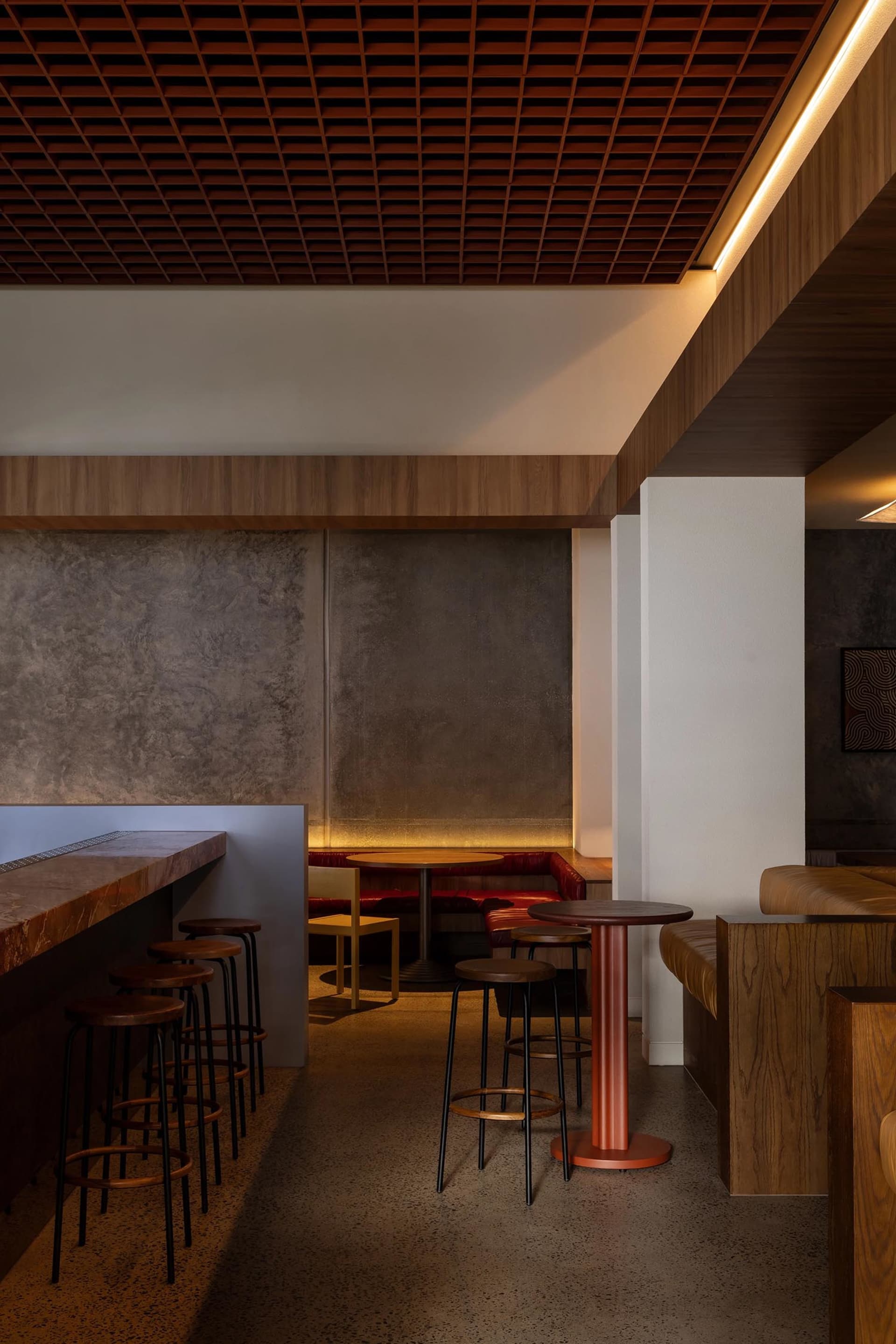Modern restaurant interior featuring wooden tables, concrete walls, and leather seating.
