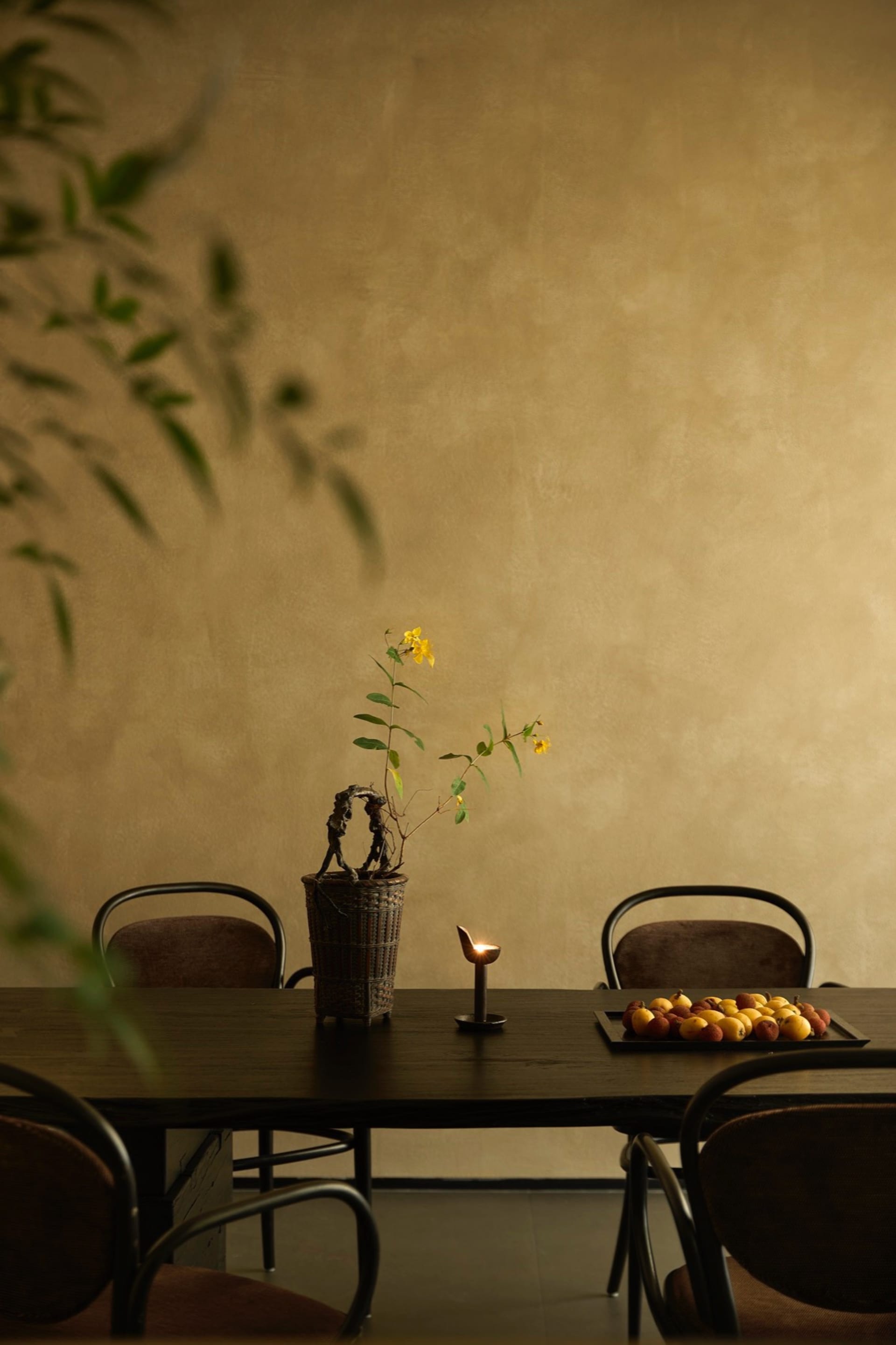 A contemporary dining room with wooden furniture, a table arrangement featuring a plant and fruits, and a warm ambiance creat