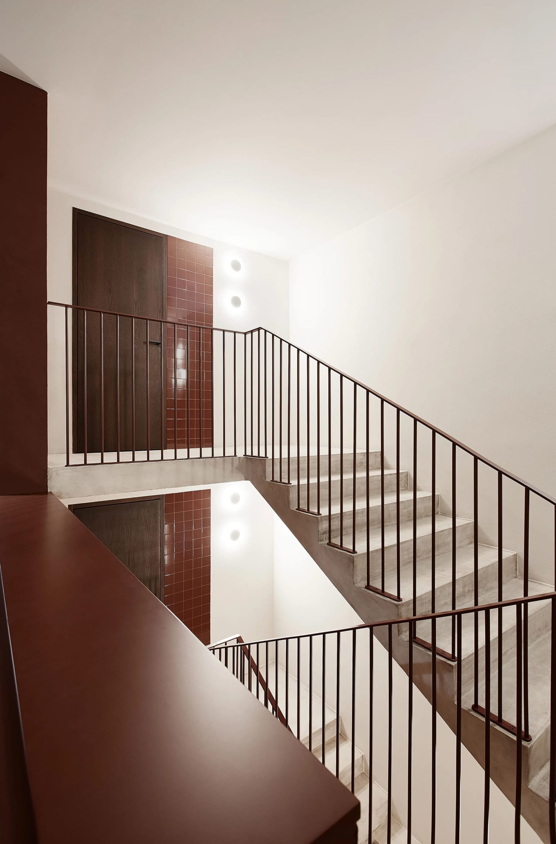 A modern interior space featuring a concrete staircase with dark railings and tiled walls.