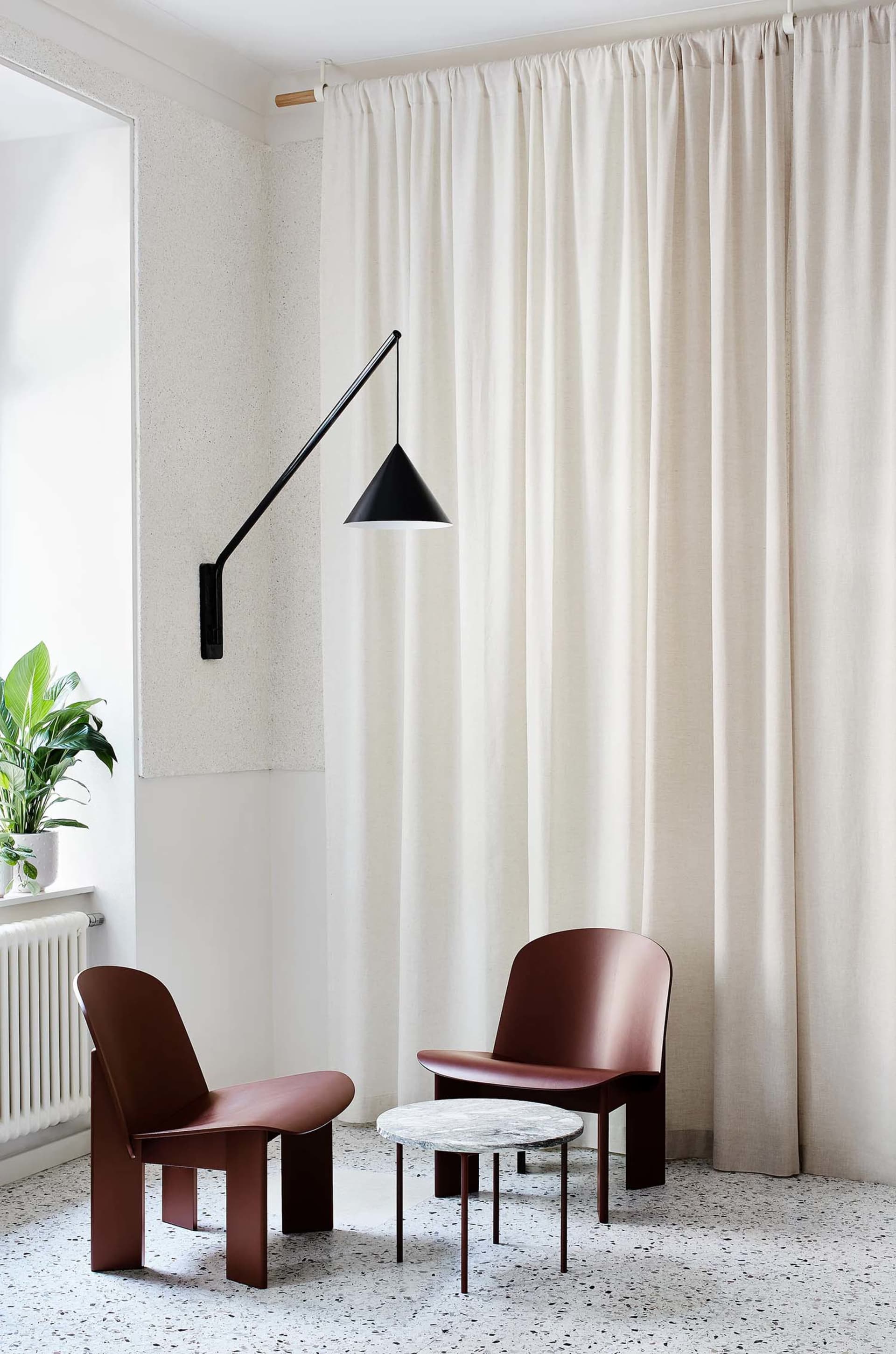 A modern lounge featuring fabric curtains, a metallic lamp shade, marble table, and resin floor.