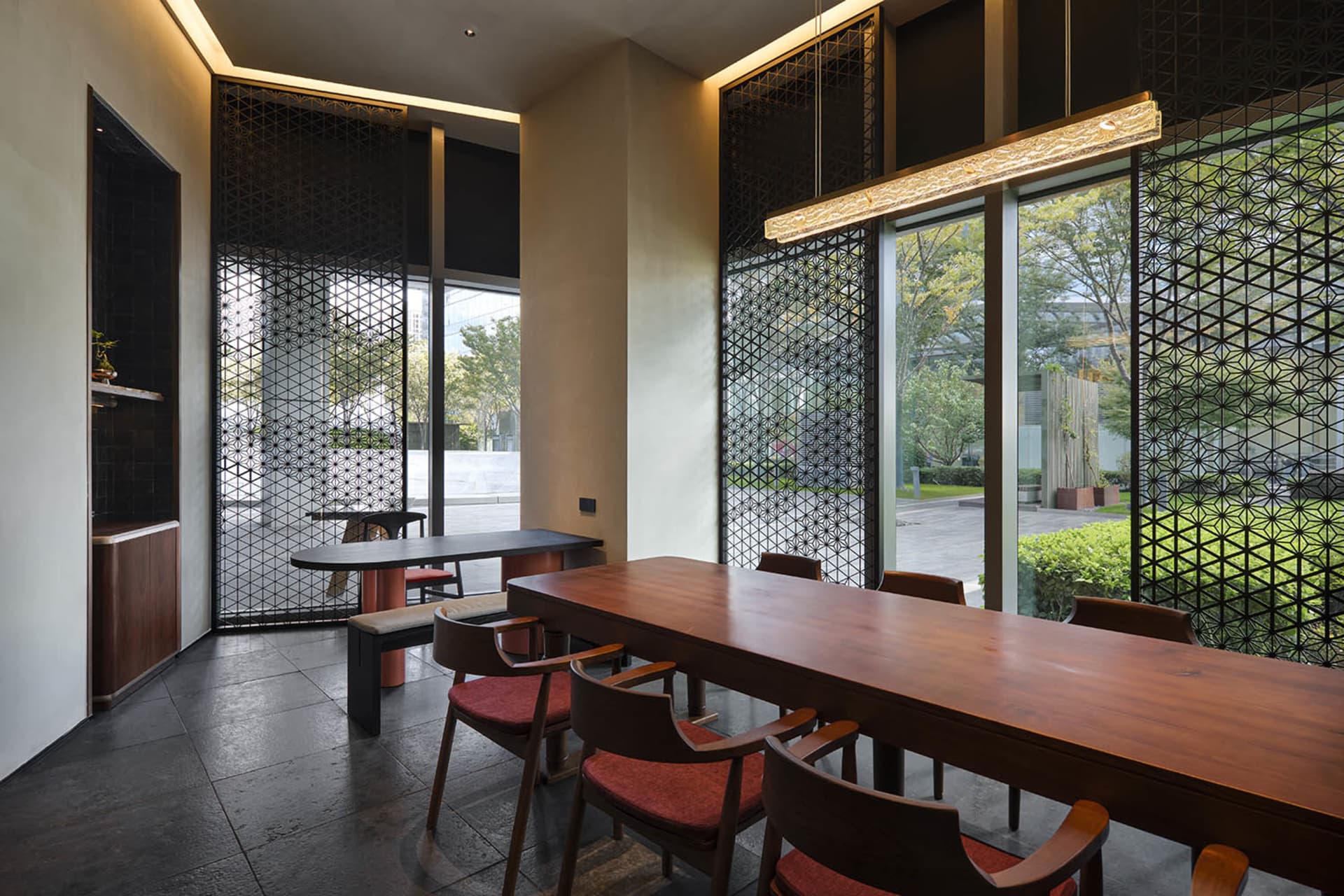 Modern restaurant interior with wooden tables, red cushioned chairs, and glass partitions.