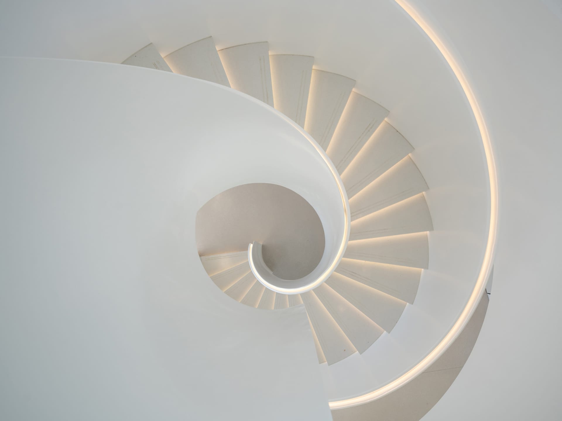 Modern, minimalist white concrete spiral staircase with illuminated edges.