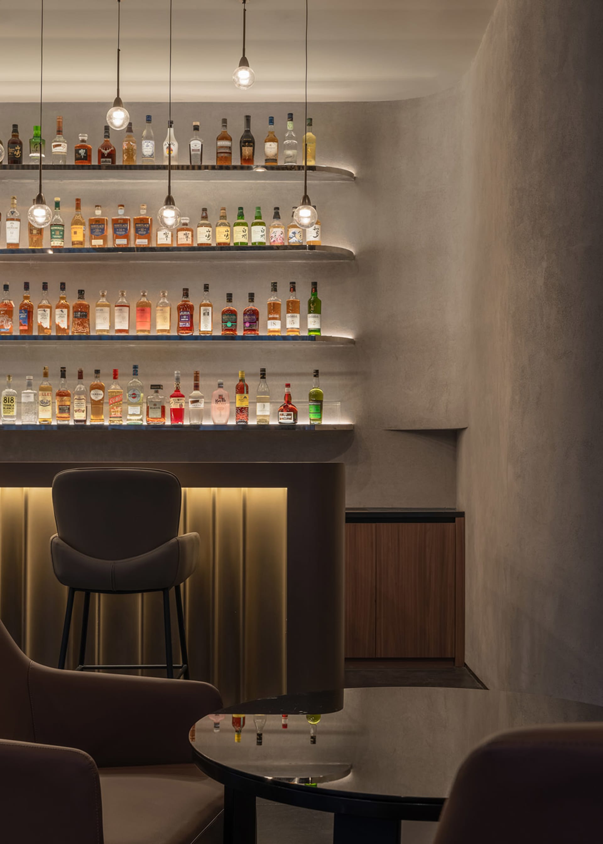 A stylish bar interior featuring concrete shelves filled with bottles of alcohol, set against a modern design backdrop with m