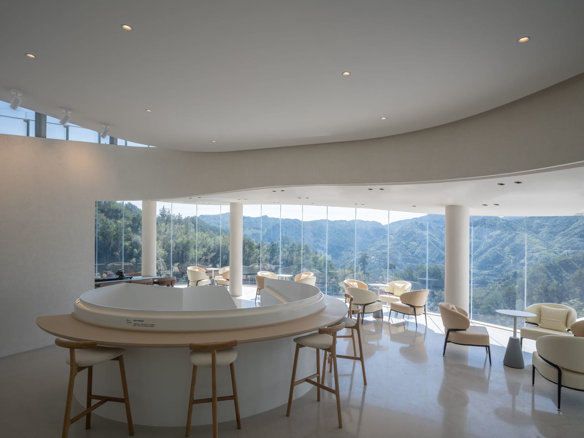 Modern cafe interior with glass walls and wooden furniture, overlooking scenic mountains.