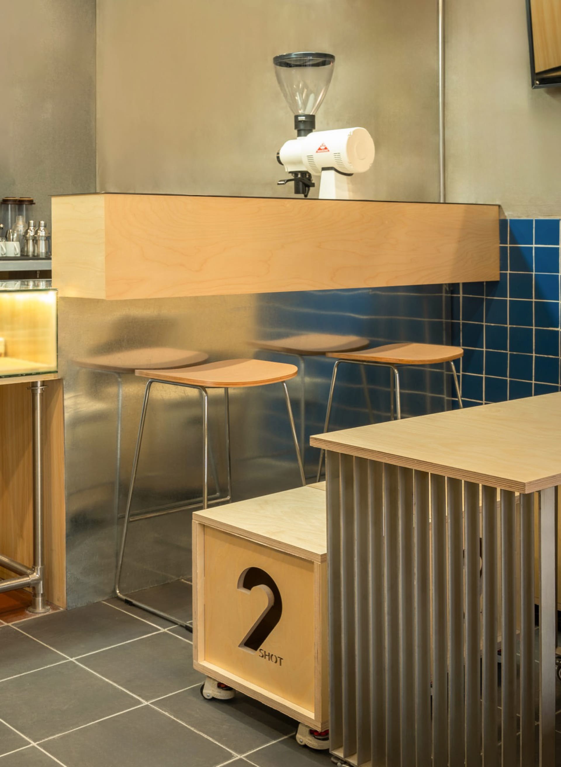 Modern wooden coffee shop bar counter with stools and espresso grinder.