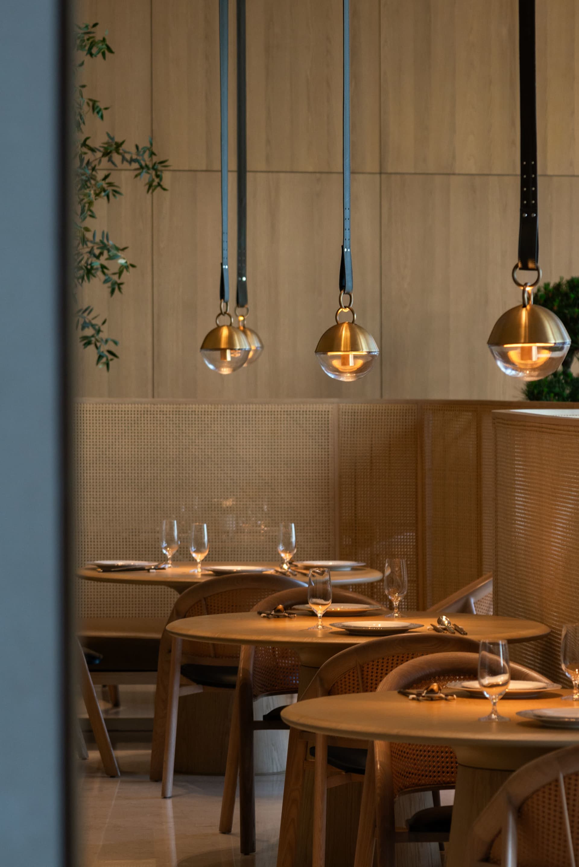 Modern restaurant dining room with wooden tables, chairs, and pendant lights.